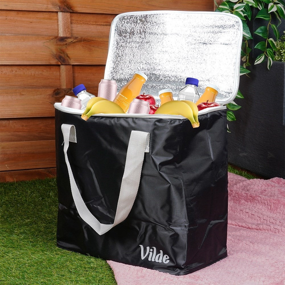 Bolsa nevera negra con frutas y bebidas, sobre una alfombra rosa.