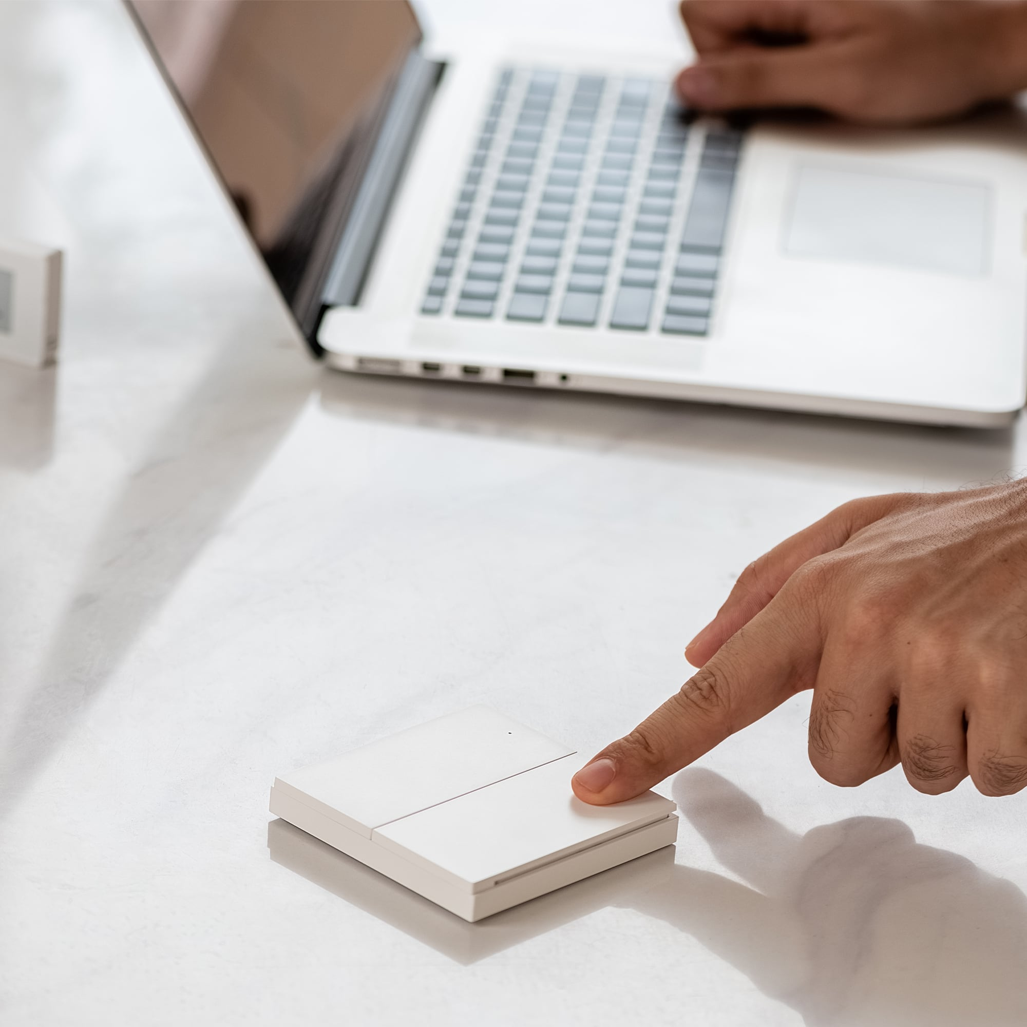 Une main appuie sur un interrupteur blanc pendant qu'une personne tape sur un ordinateur portable.