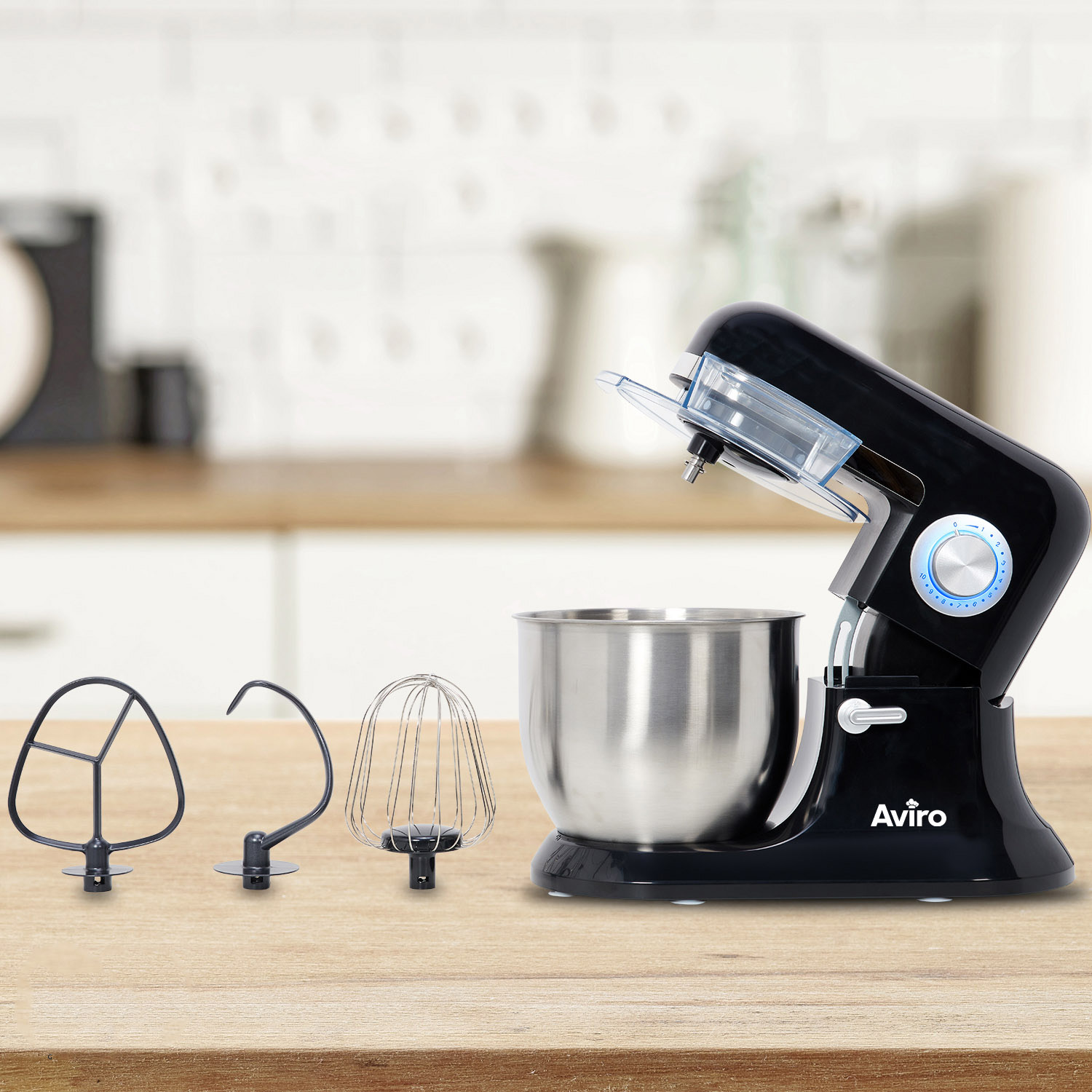Black kitchen mixer with stainless steel bowl and three attachments on a wooden table.