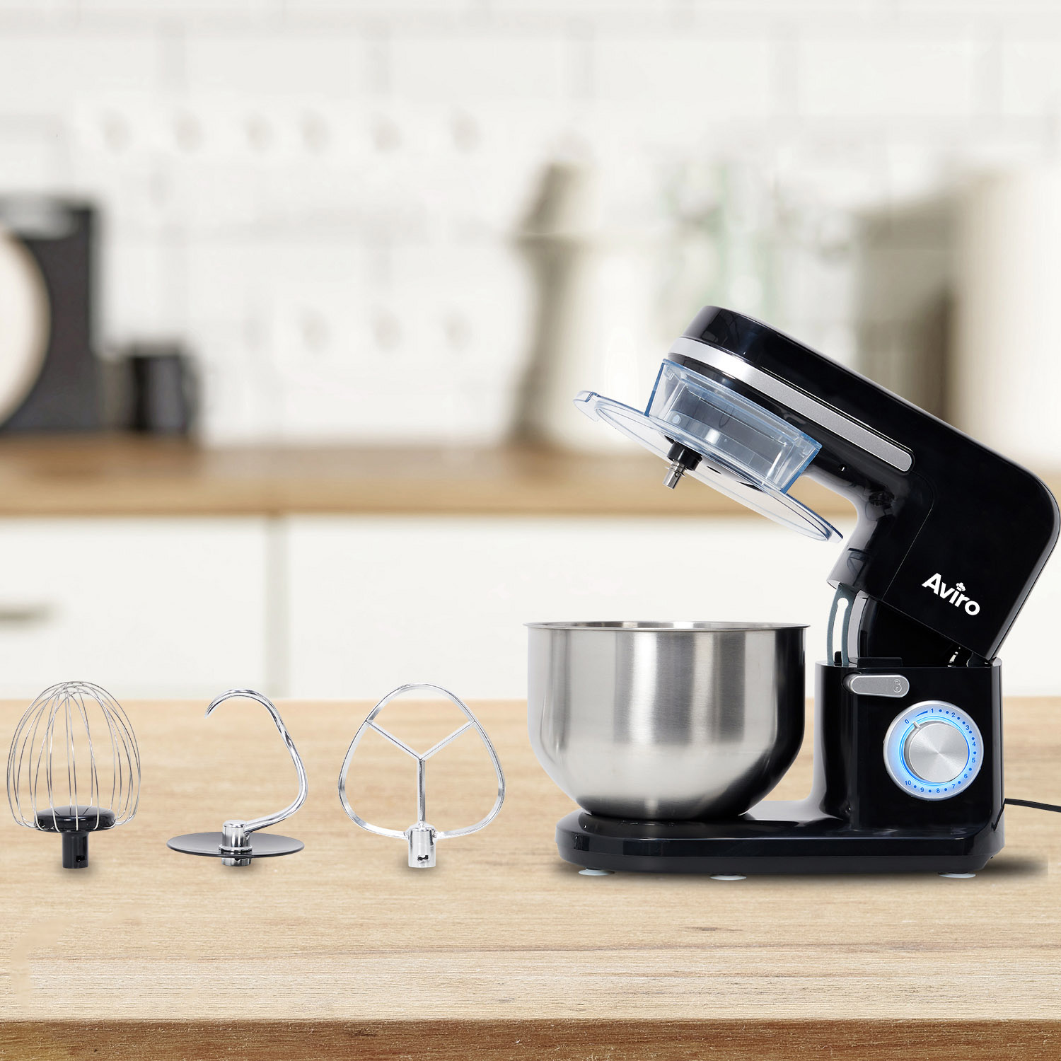 Black stand mixer with stainless steel bowl and three attachments on a wooden table.