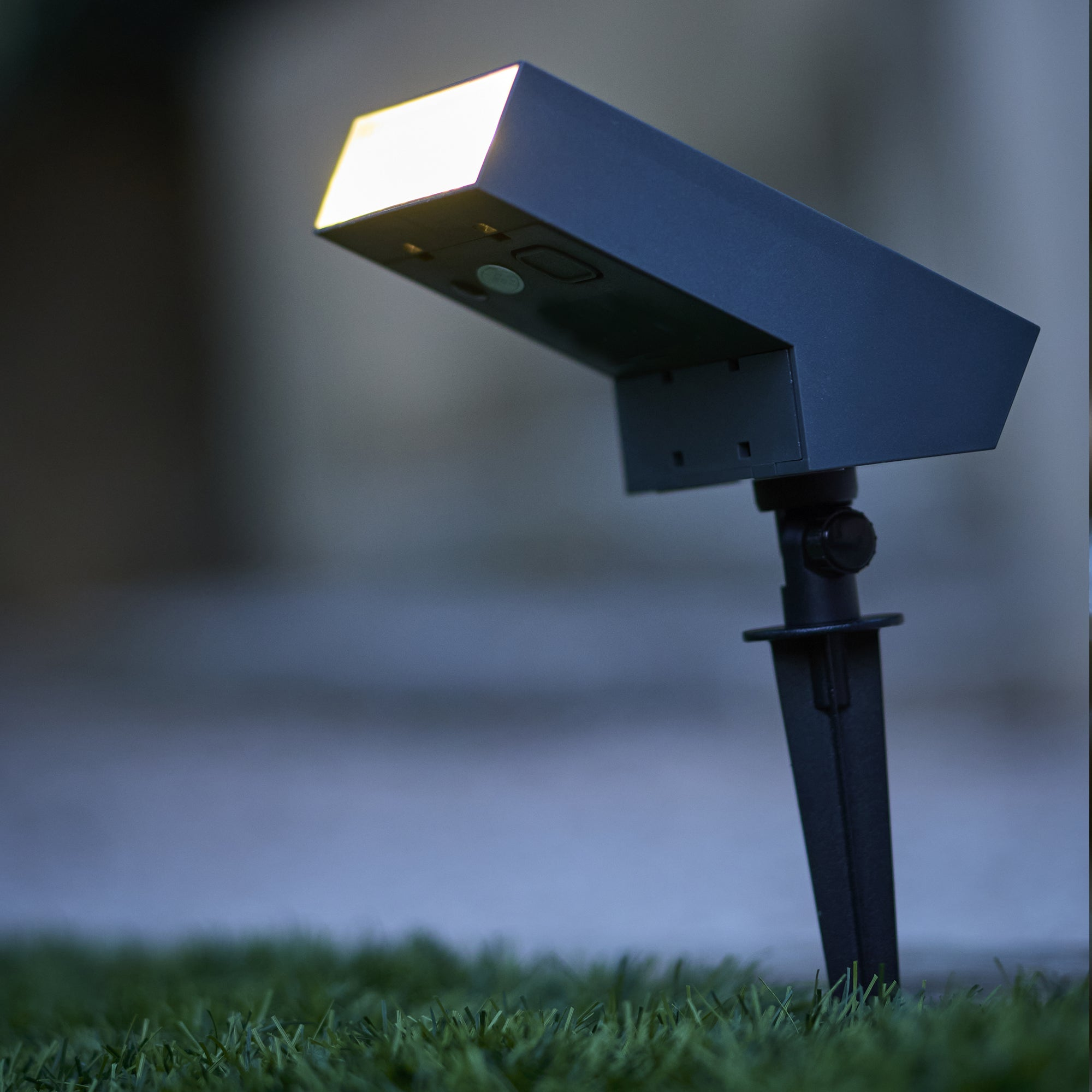 Ein dunkler Außenstrahler mit hellem Licht steht auf Rasen.
