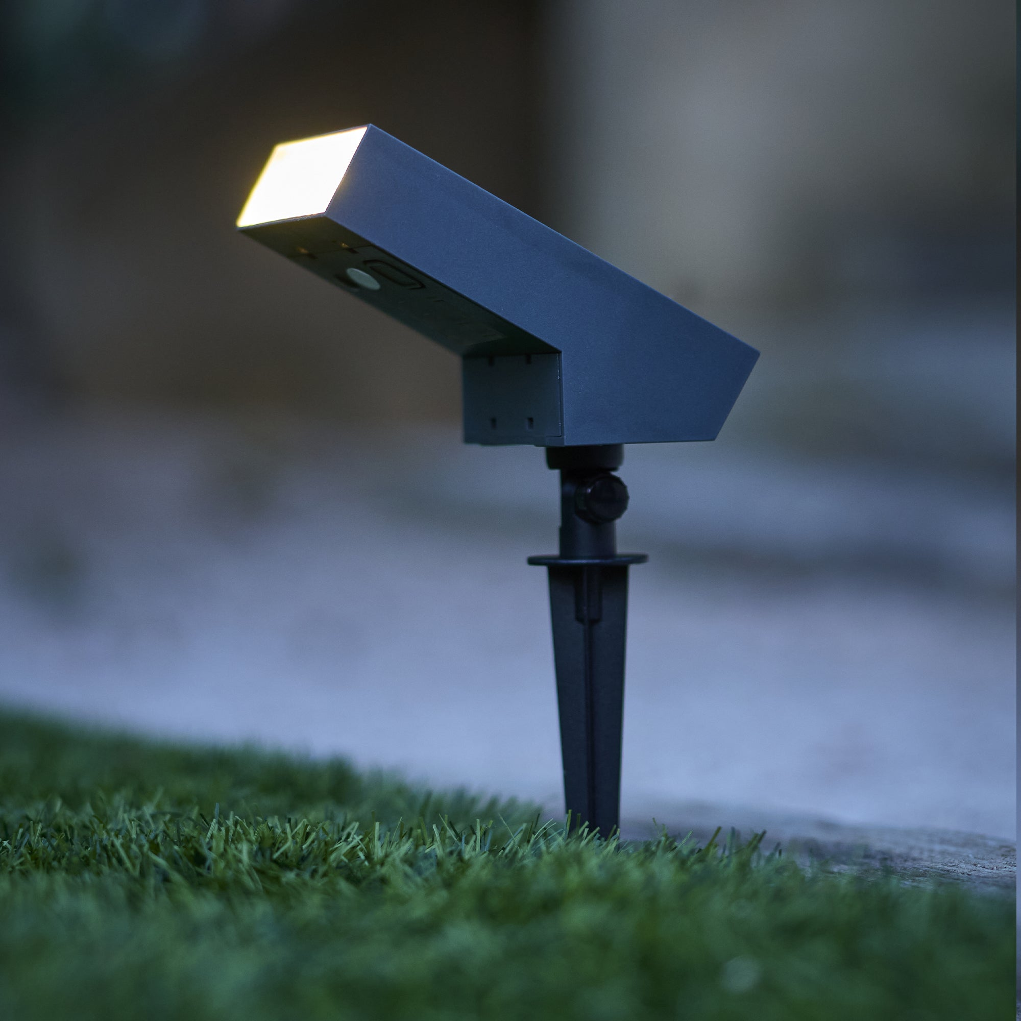 Eine dunkle Solarleuchte mit hellem Licht steht im Gras.