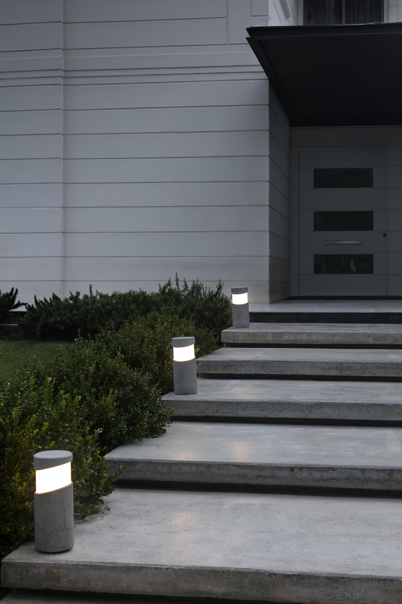 Gradini in cemento verso una casa con tre luci e cespugli.