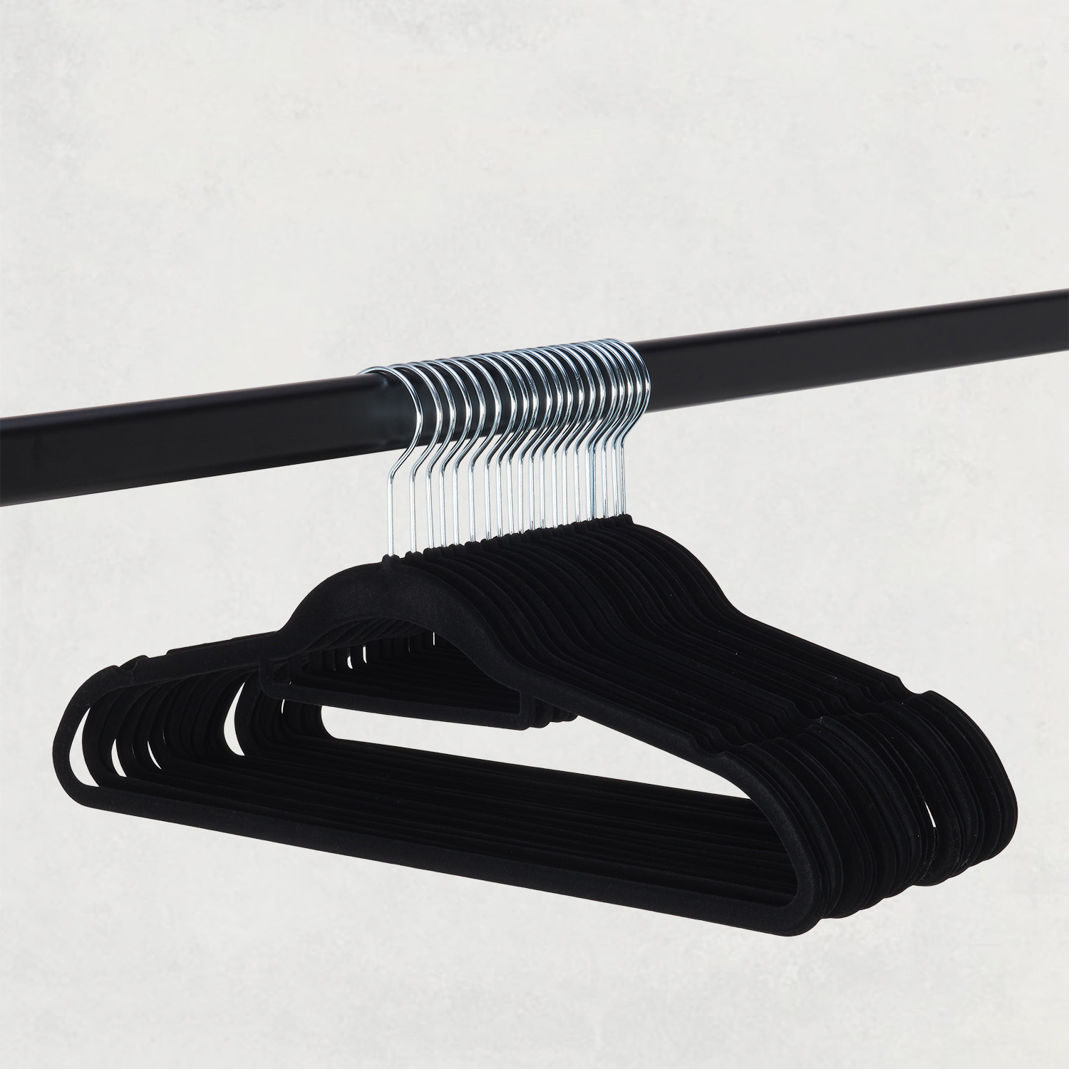 Een groep zwarte fluwelen hangers hangt aan een zwarte stang.