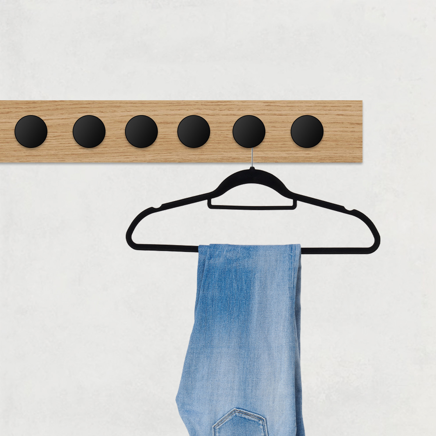 Blauwe jeans hangen aan een zwarte hanger aan een houten rek met zwarte knoppen.