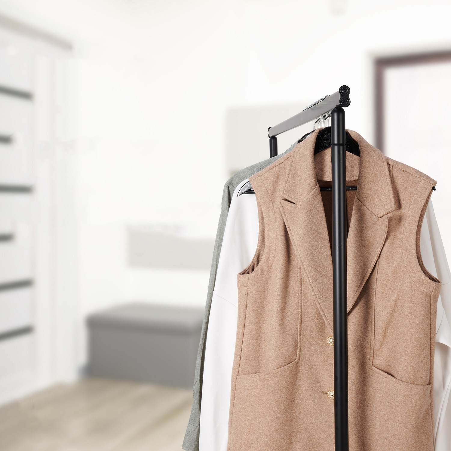Een beige damesvest over een wit shirt hangt aan een kledingrek in een hal.