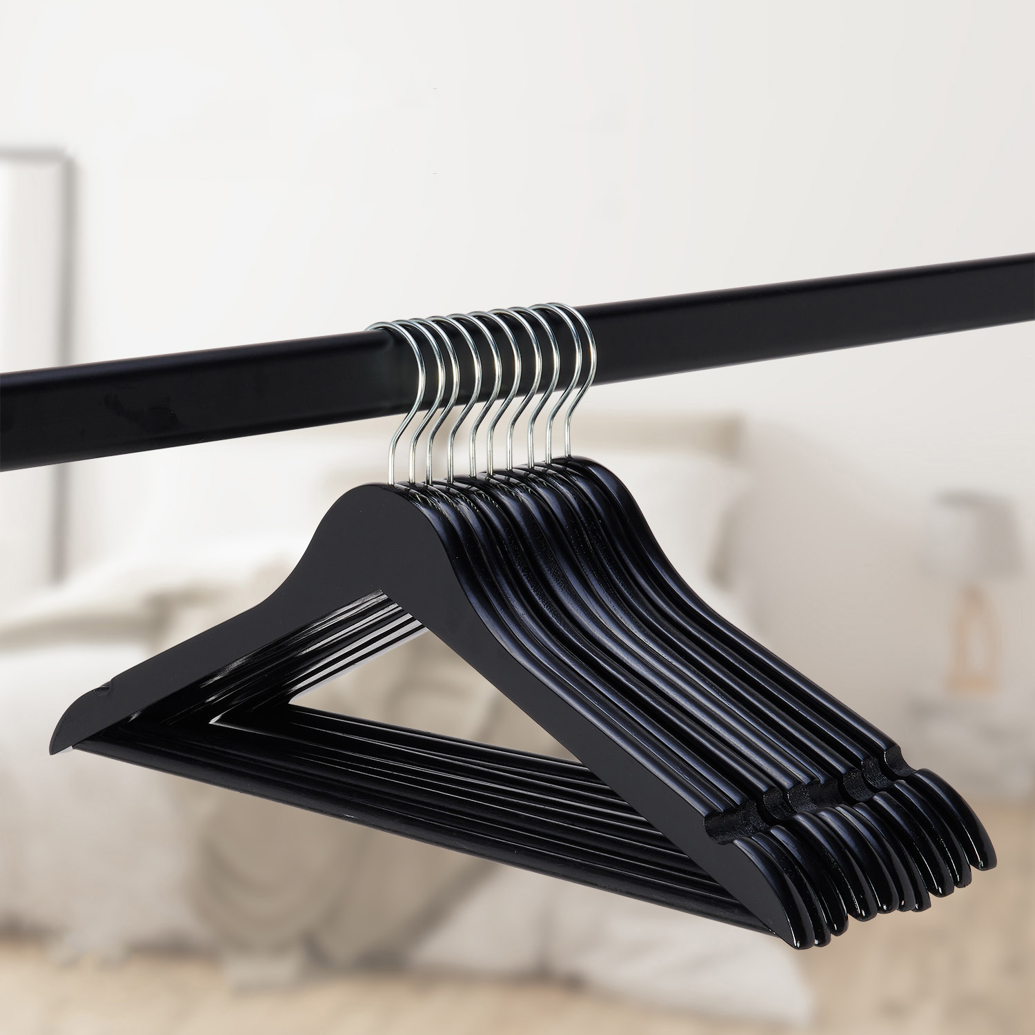 Een rij zwarte houten kledinghangers hangt aan een staaf voor een vage slaapkamerachtergrond.