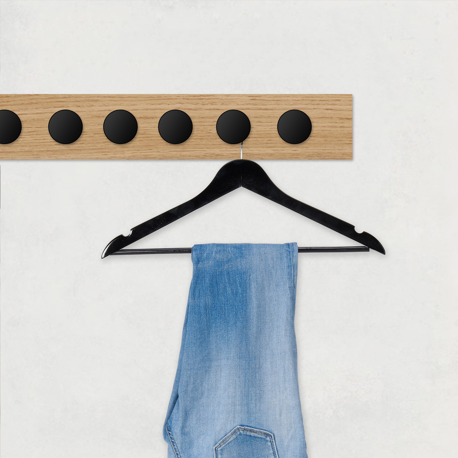 Een houten kapstok met zes zwarte knoppen, met een zwarte hanger met een blauwe spijkerbroek.