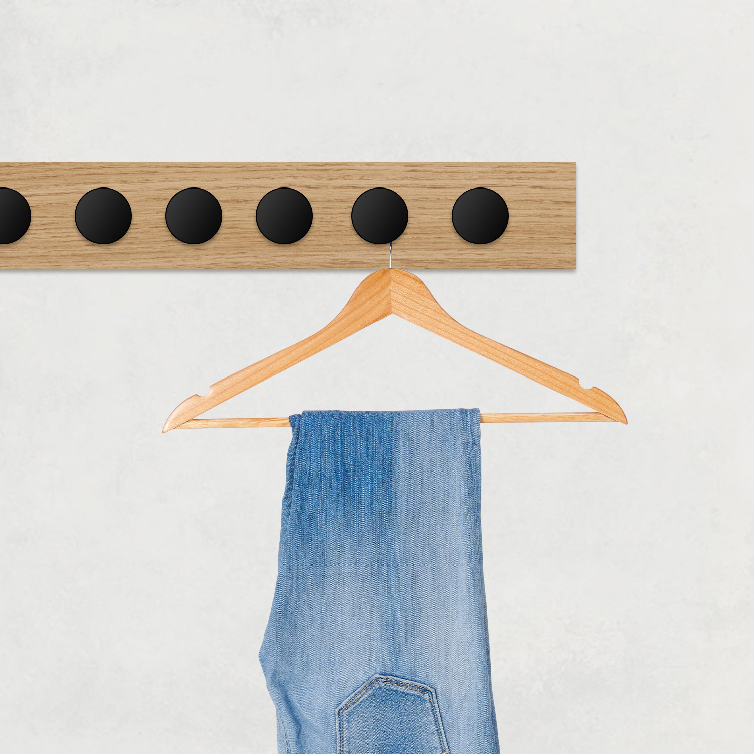 Blauwe spijkerbroek hangt aan een hanger aan een houten rek met zwarte knoppen.