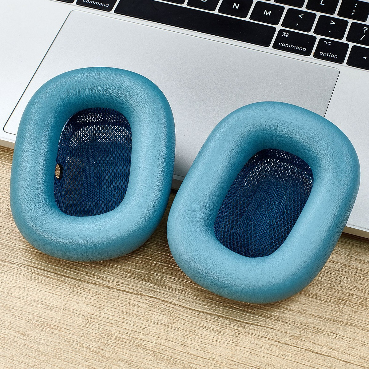Zwei hellblaue Kopfhörerpolster liegen auf einer Tastatur und einem Holztisch.