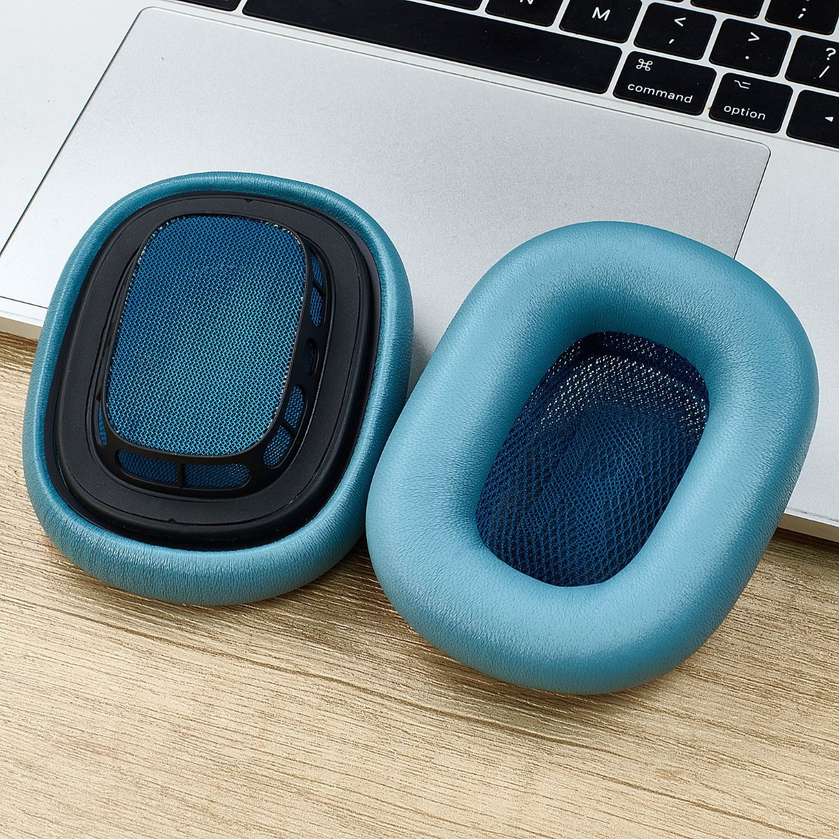 Zwei blaue Kopfhörerpolster liegen auf einem Laptop und Holztisch.