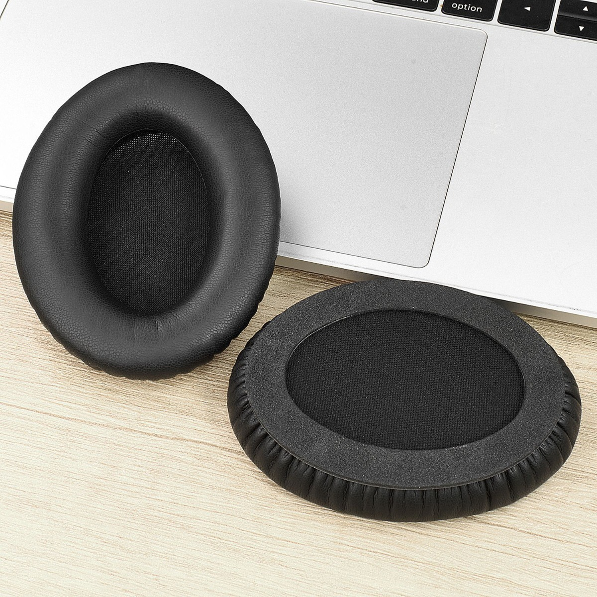 Due cuscinetti auricolari neri su una scrivania di legno accanto a un laptop.