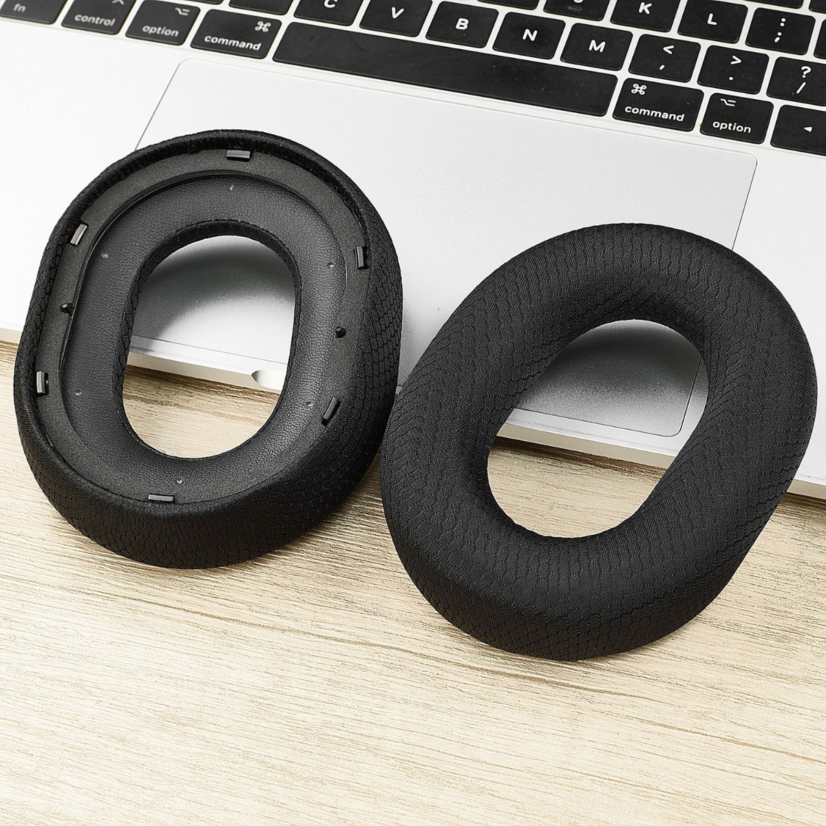Due cuscinetti neri per cuffie riposano su una tastiera di laptop e legno.