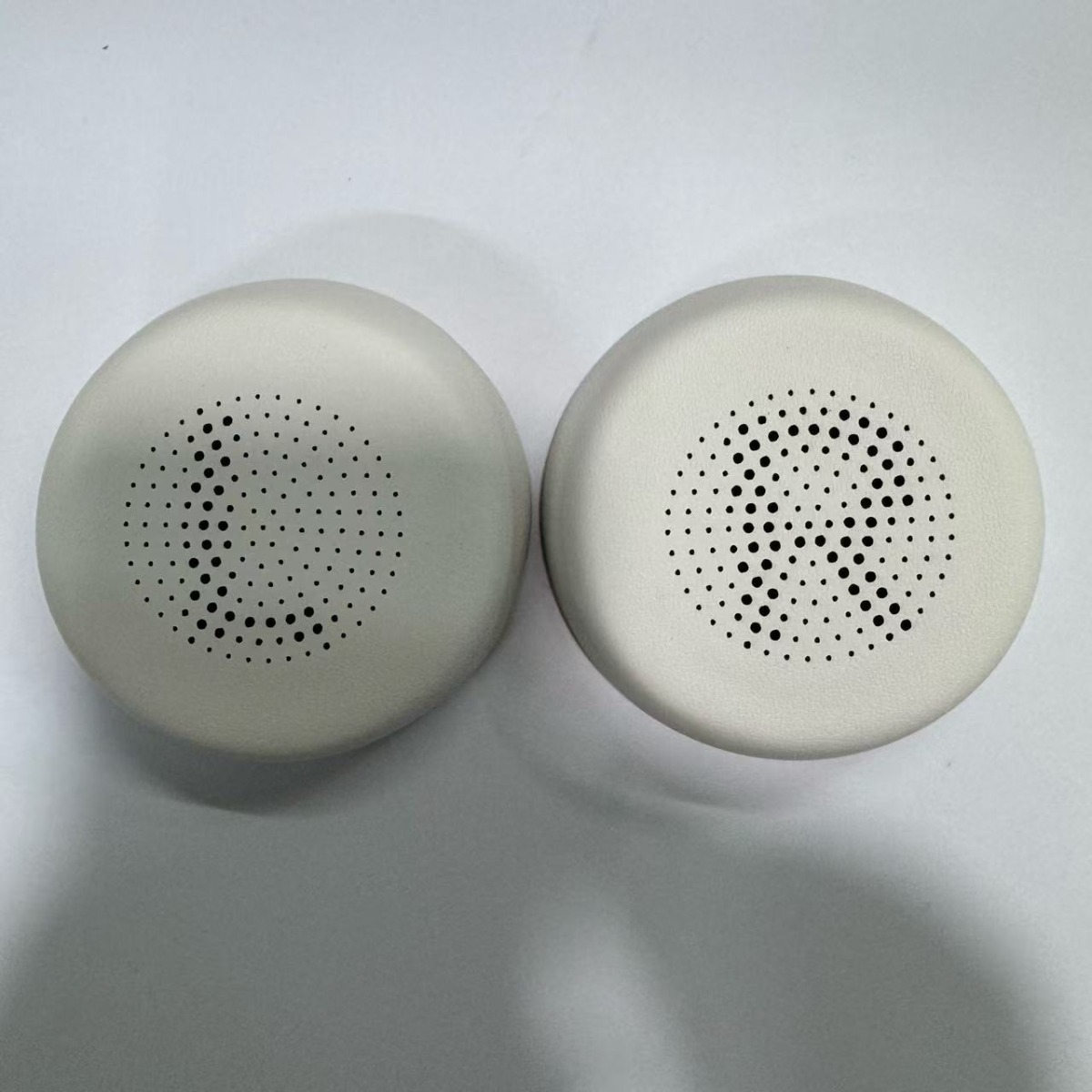 Due cuscinetti auricolari bianchi con griglie altoparlanti forate.