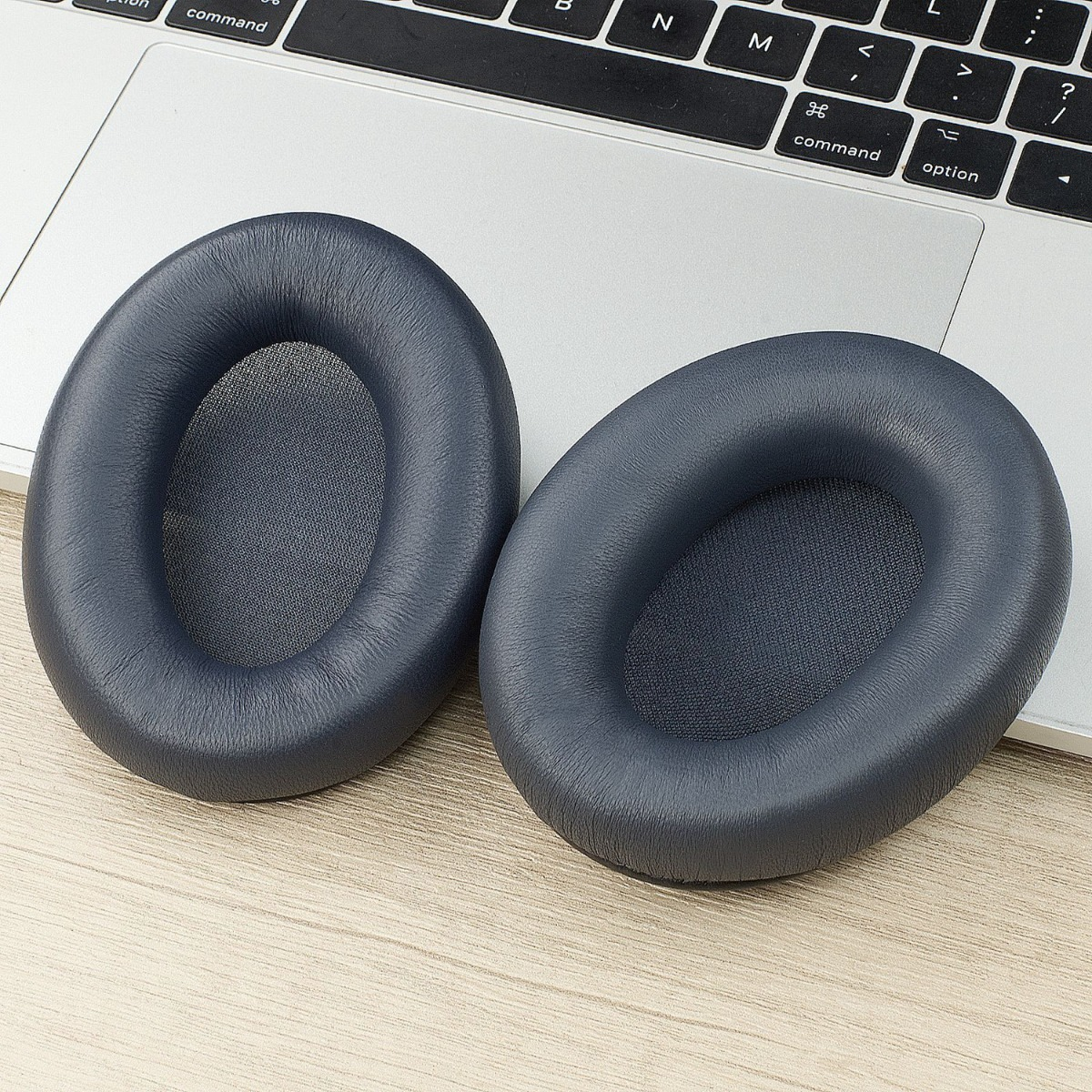 Due cuscinetti auricolari blu scuro su un tavolo di legno accanto a una tastiera di laptop.