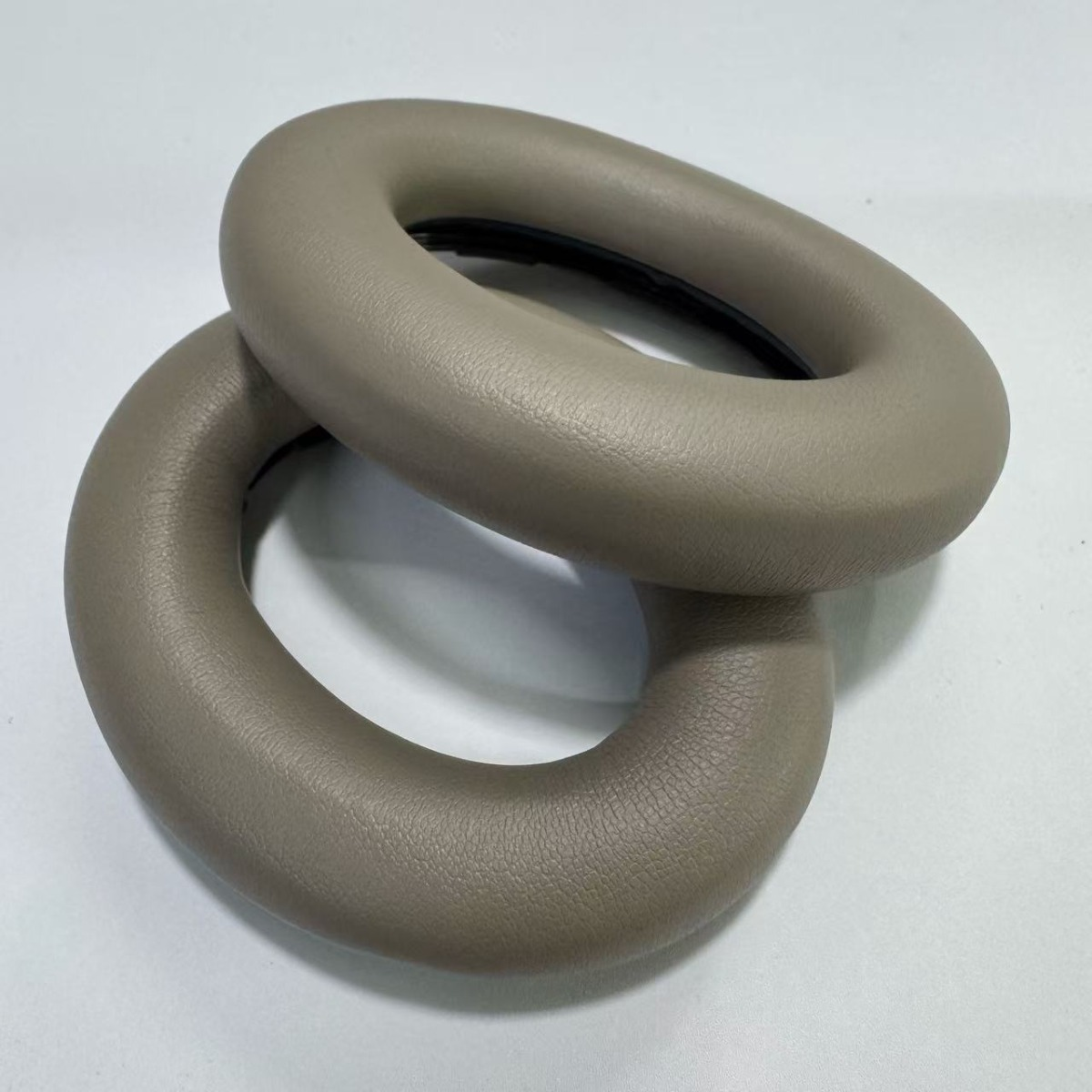 Due paraorecchie beige per cuffie sono impilati su una superficie bianca.