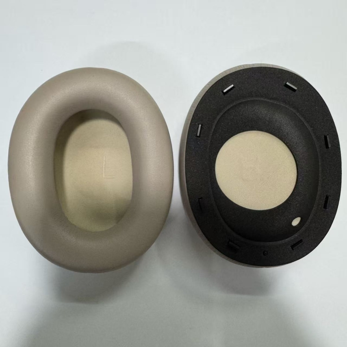 Zwei Ohrpolster für Kopfhörer, eines beige mit 'L', das andere schwarz mit beige Polster.