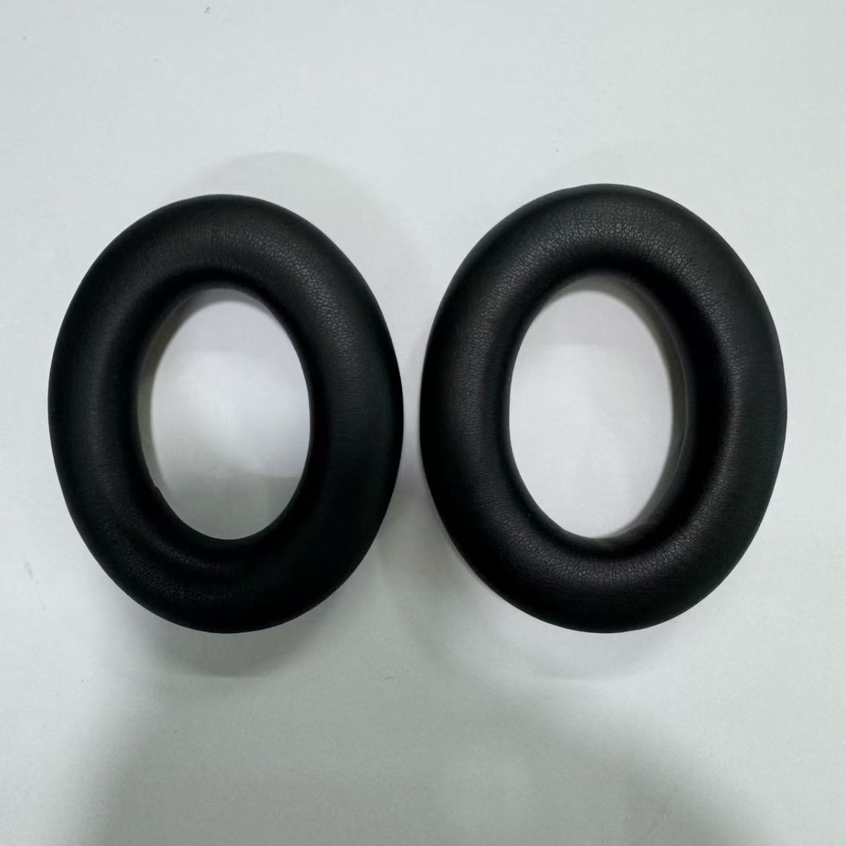 Two black, oval ear pads lie next to each other on a white surface.