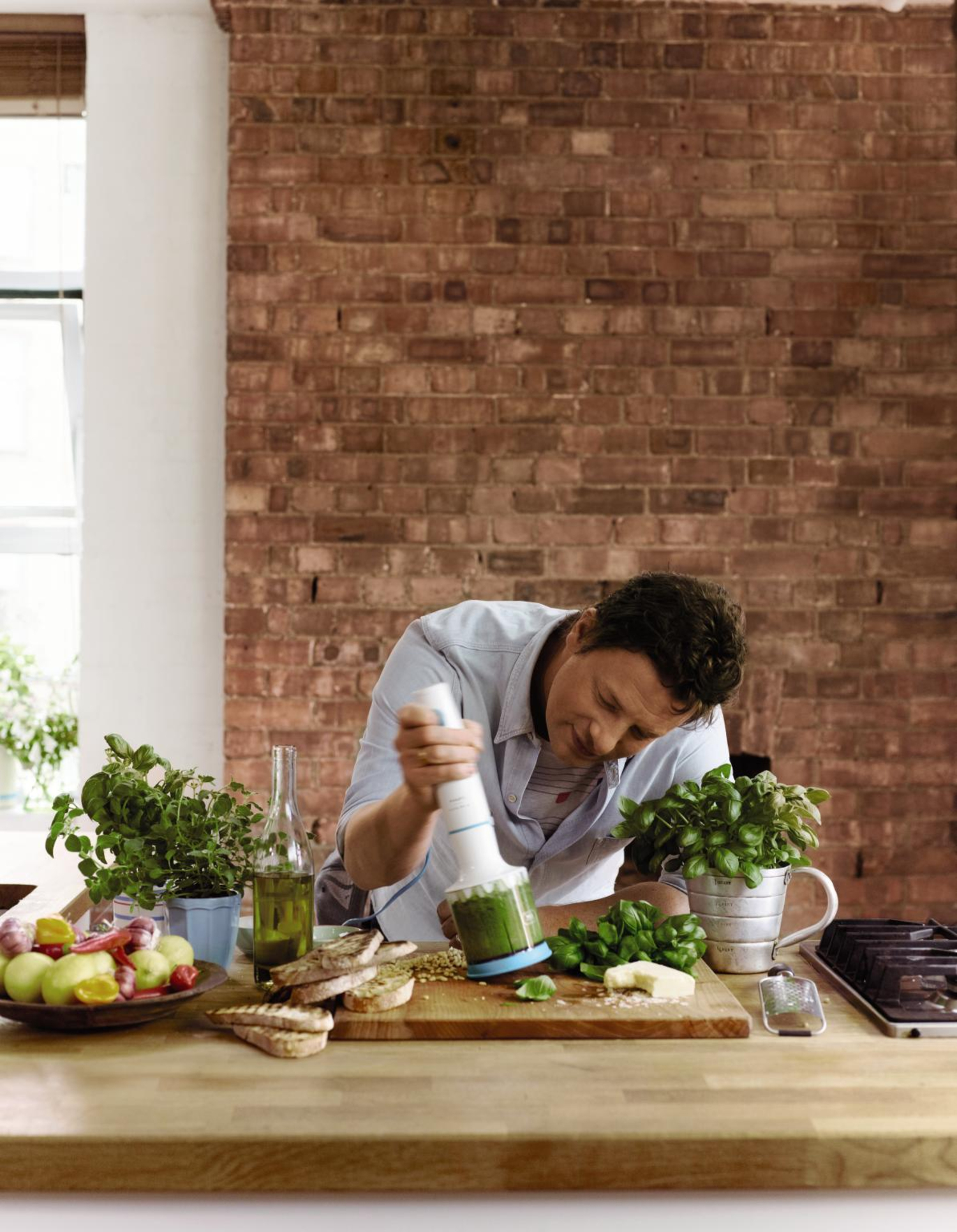 Uomo in cucina frulla pasta verde con frullatore a immersione vicino a basilico e pane.