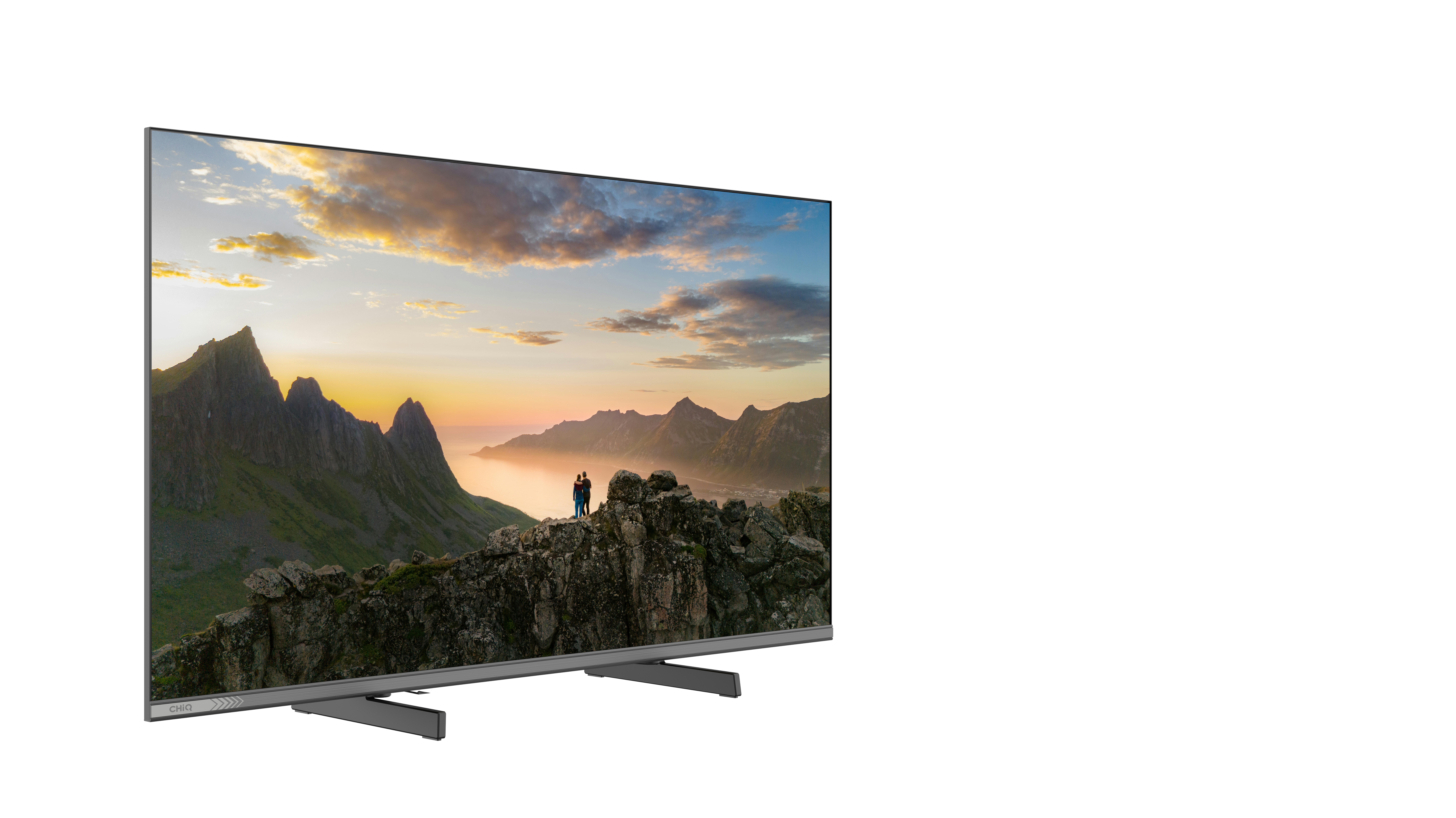 Telewizor wyświetla górski krajobraz o zachodzie słońca z dwiema osobami.