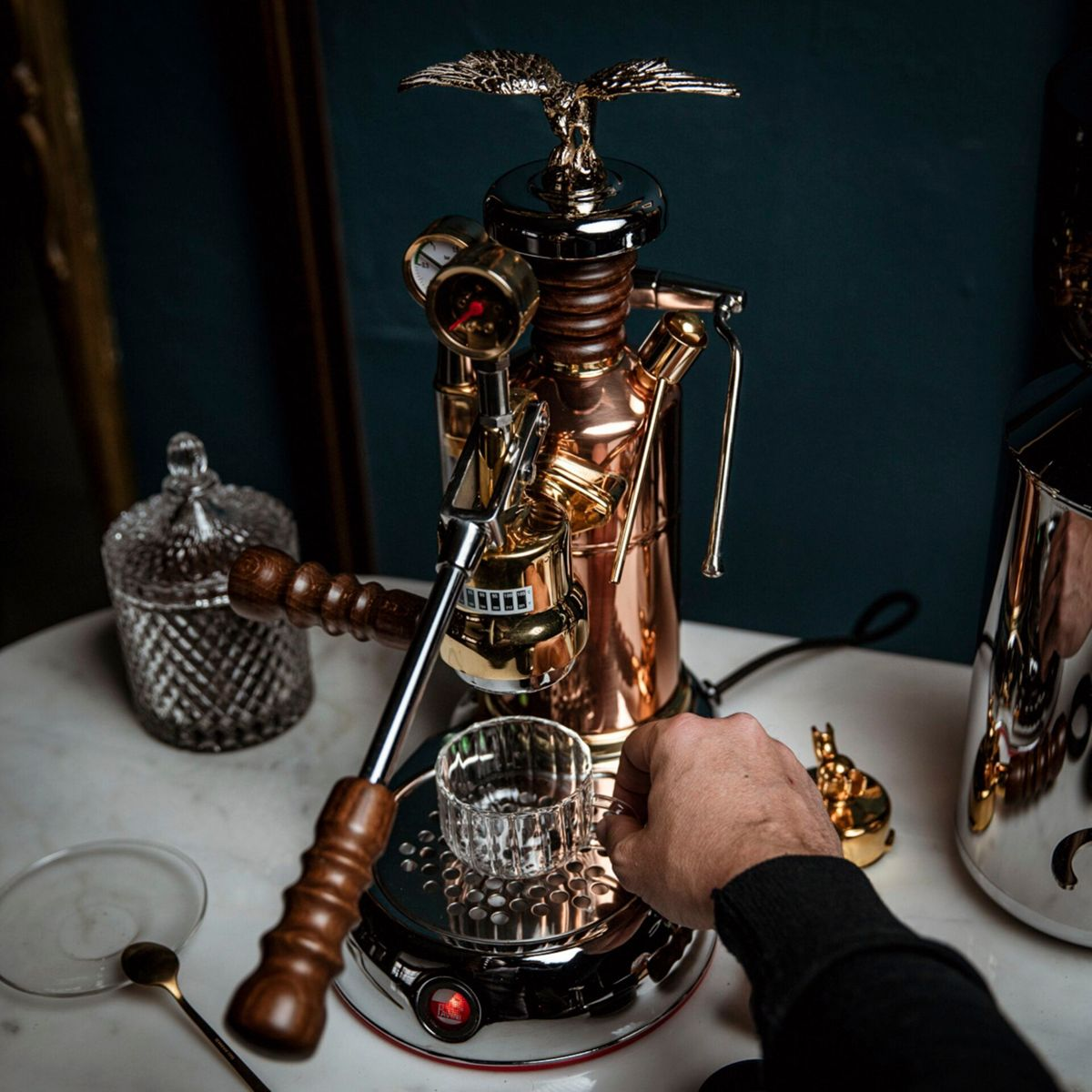Miedziany ekspres do kawy z orłem, szklanką i ręką.