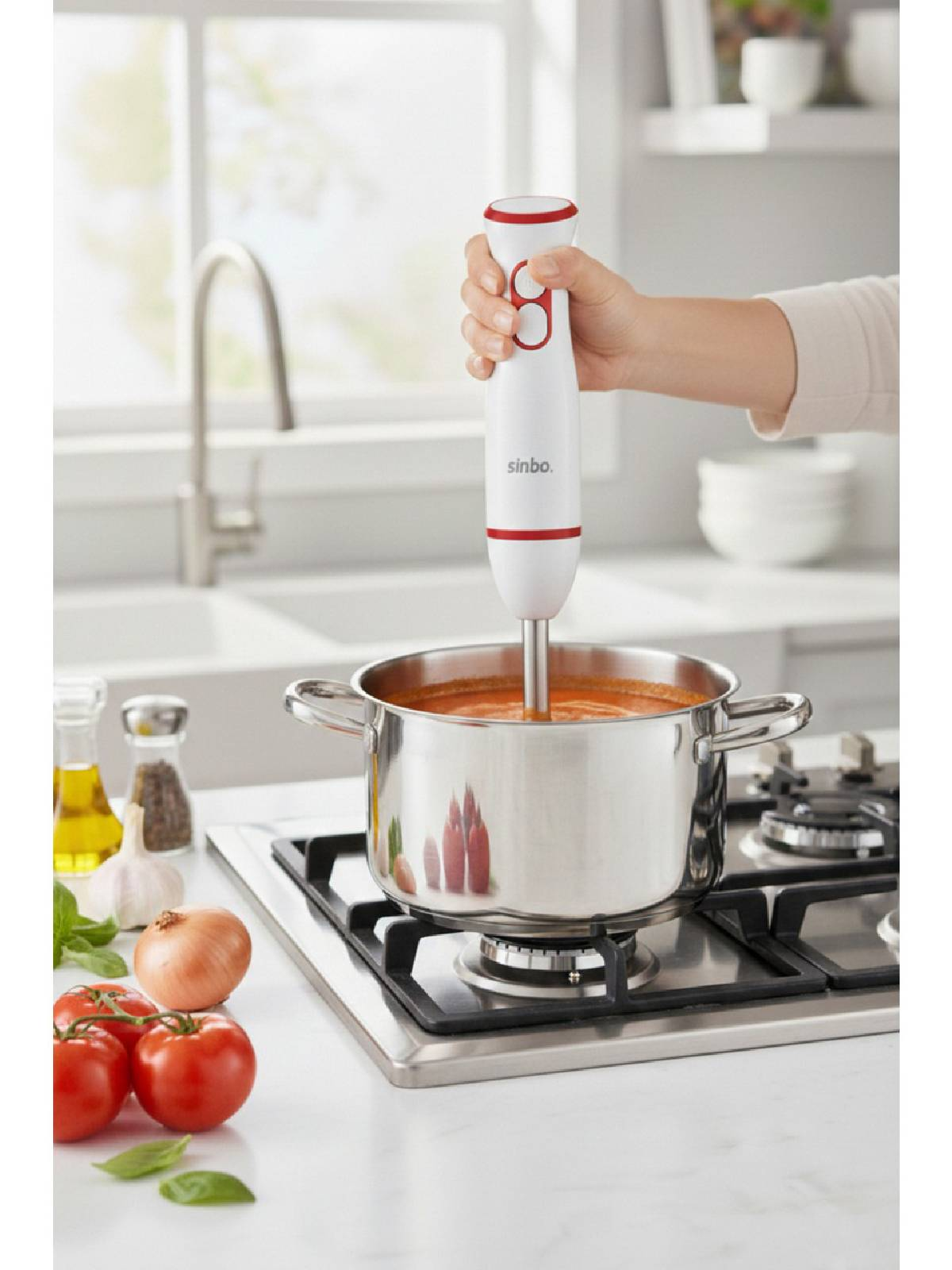 Bir el, ocaktaki domates çorbası tenceresinin üzerinde el blenderı tutuyor.