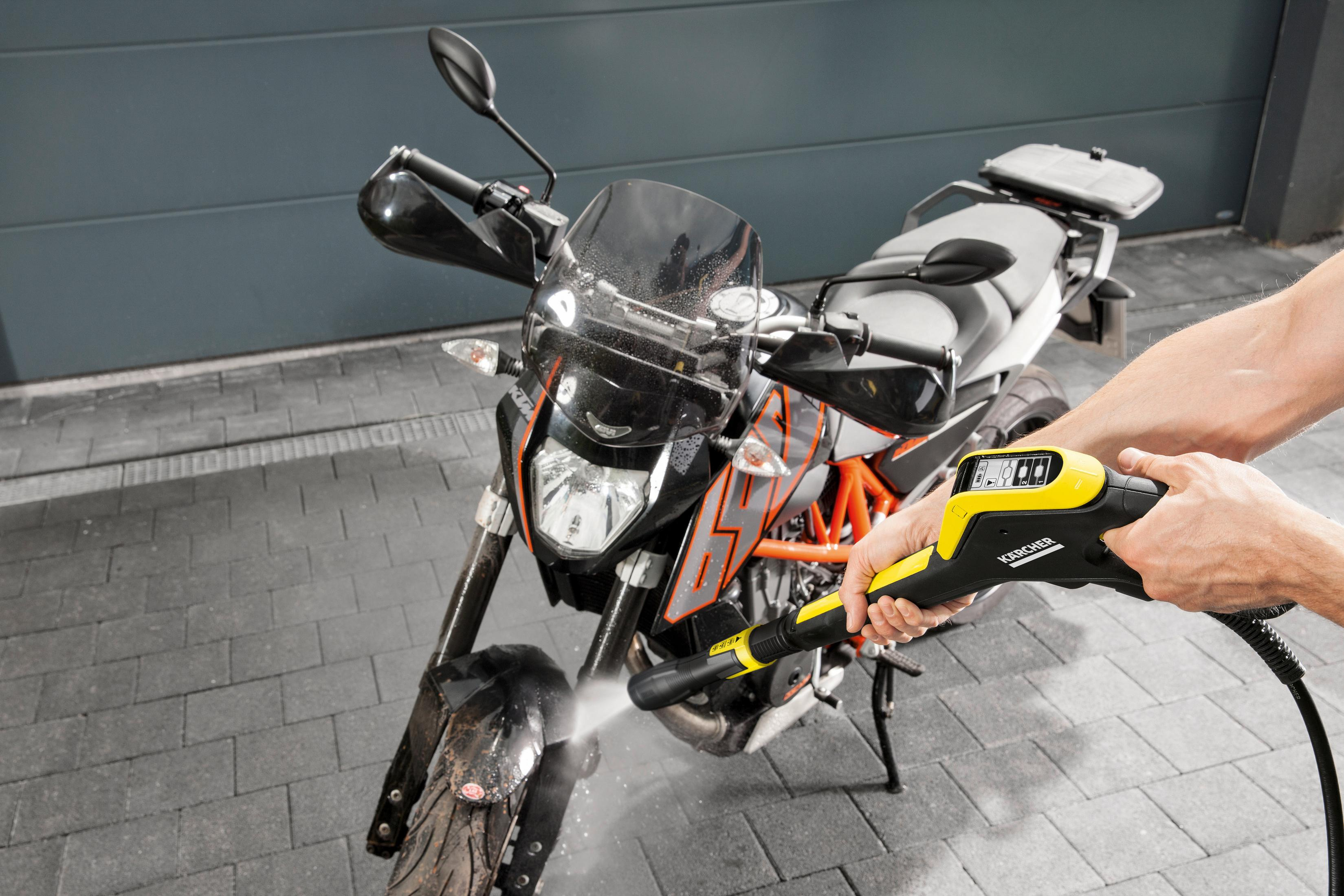 Un uomo lava una moto con un'idropulitrice davanti a una porta del garage.