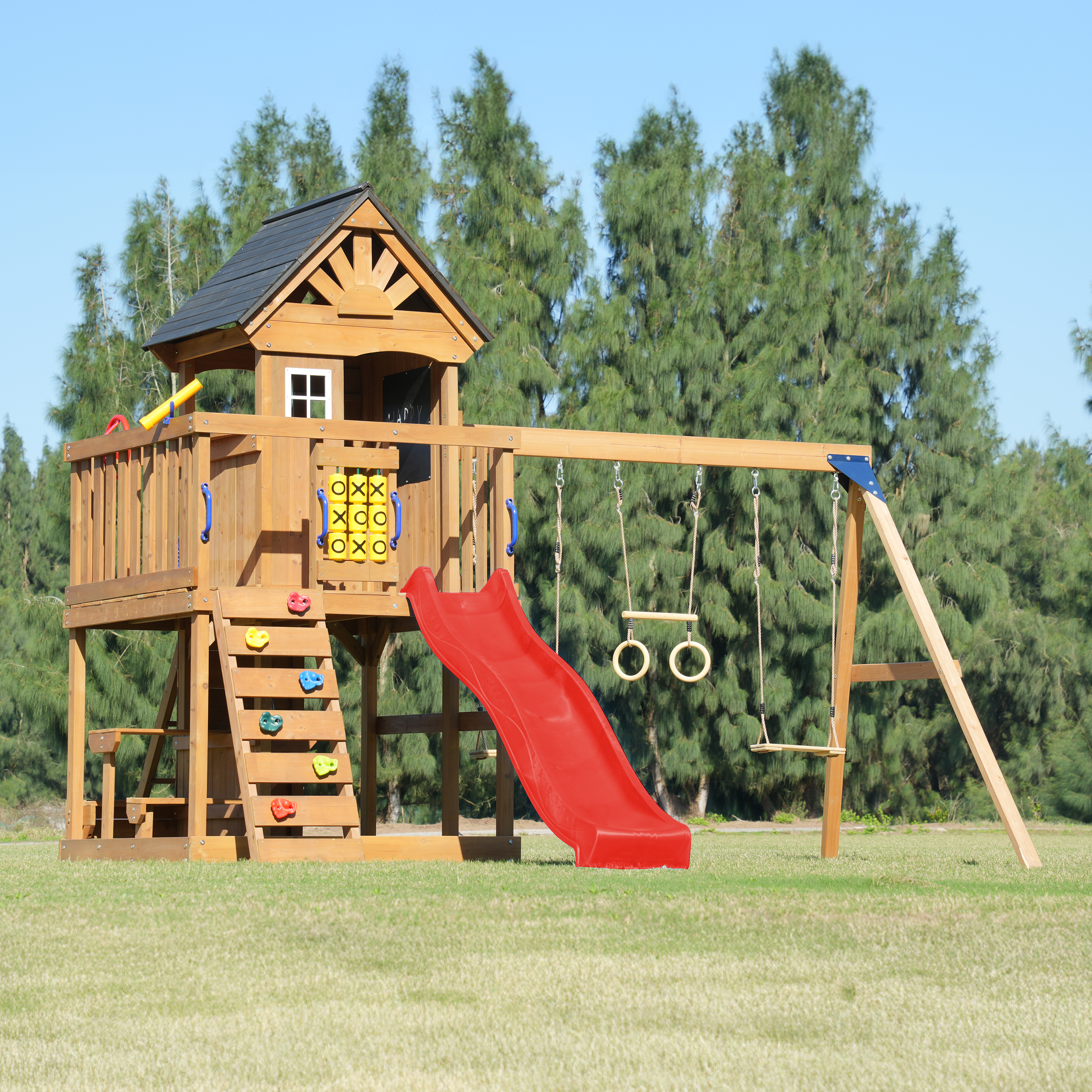 Holzspielturm mit roter Rutsche, Schaukeln und Kletterwand auf Gras.