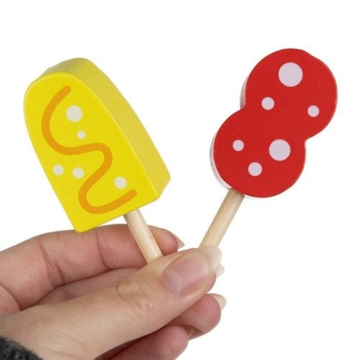 Una mano sostiene dos juguetes de madera: un helado amarillo y una seta roja.