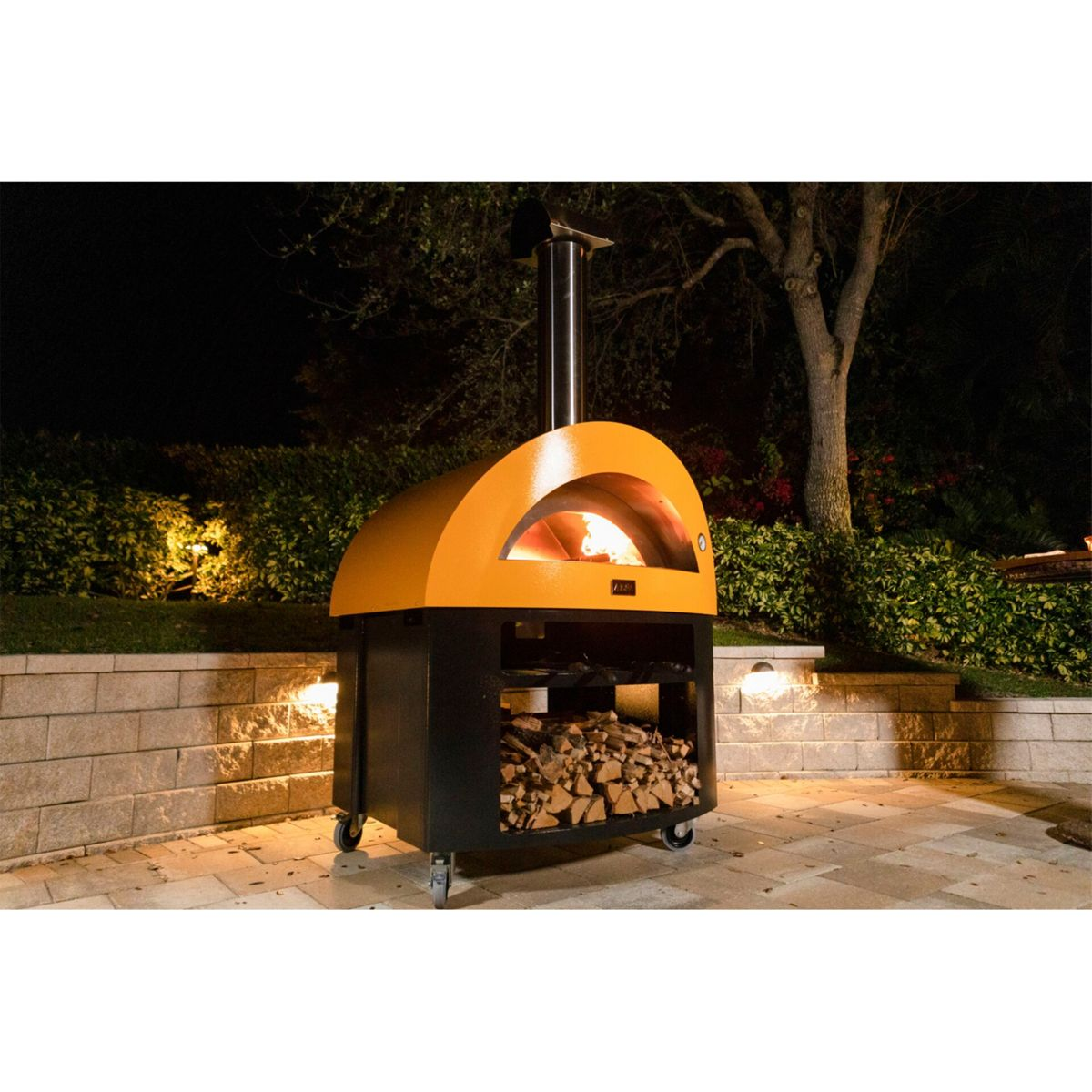 Ein orangefarbener Pizzaofen mit brennendem Feuer und Holz im Freien bei Nacht.