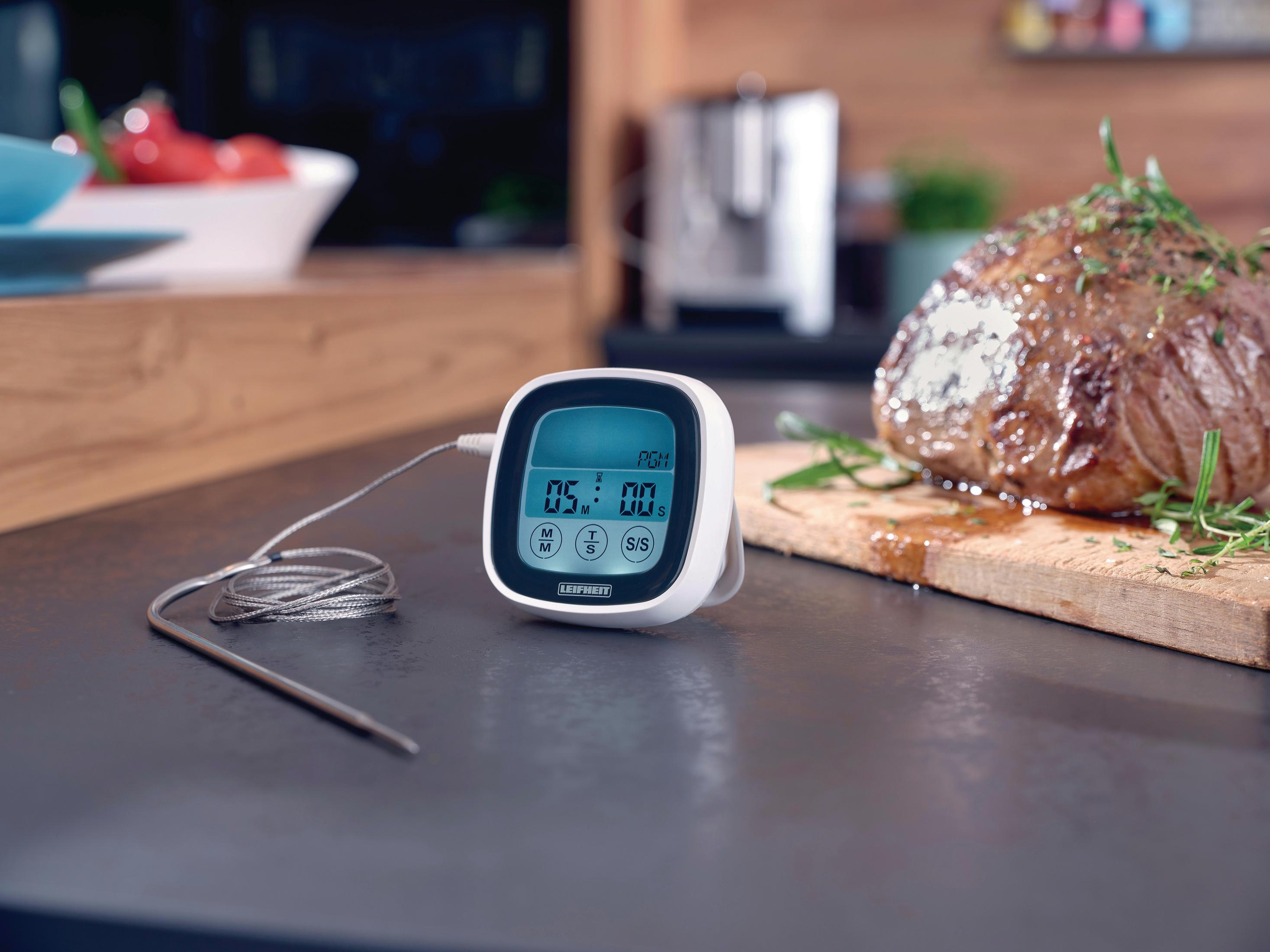 Ein digitaler Fleischthermometer mit Kabel liegt neben einem gebratenen Braten auf einem Holztisch.