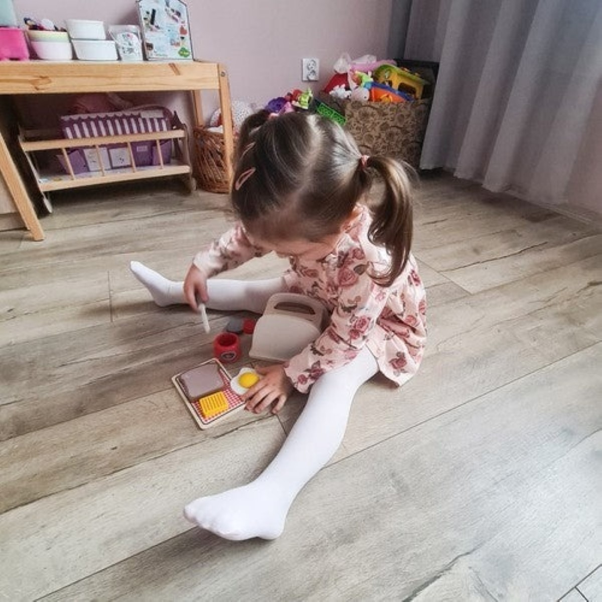 Una niña juega con una tostadora de juguete y comida en el suelo.