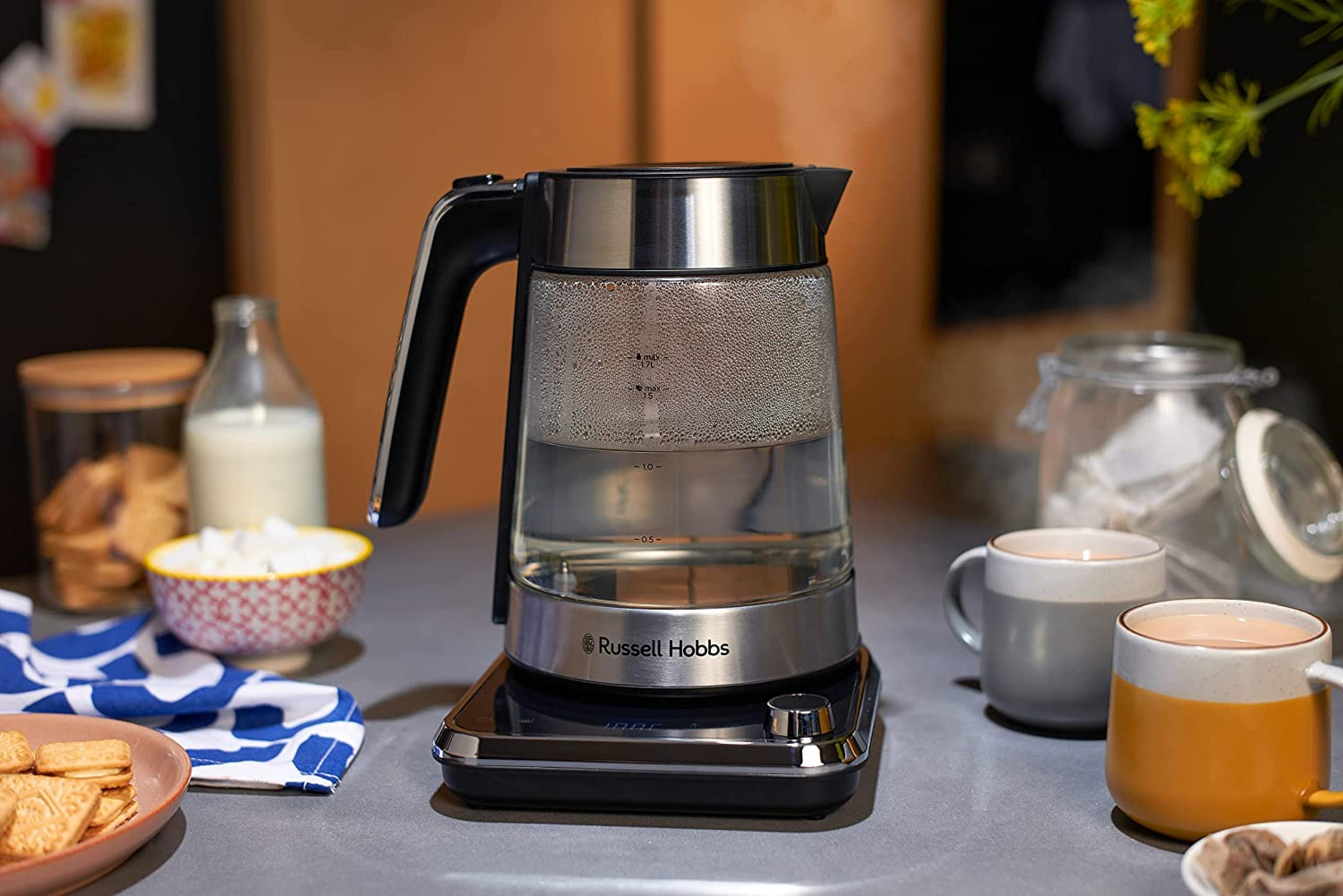 Une bouilloire en verre est sur un socle. Deux tasses sont à proximité.