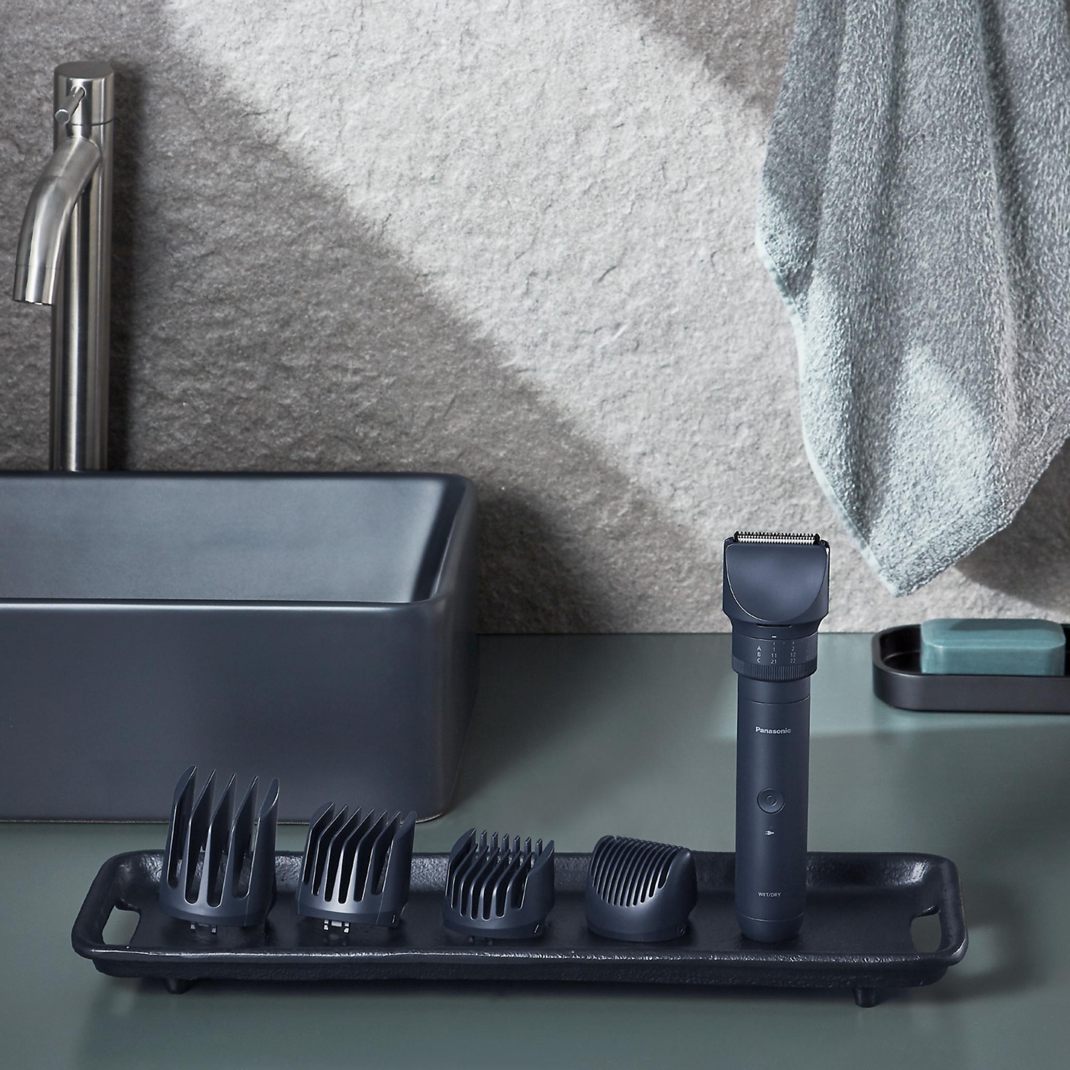 Ciemna maszynka do strzyżenia włosów z nasadkami na tacy w łazience.