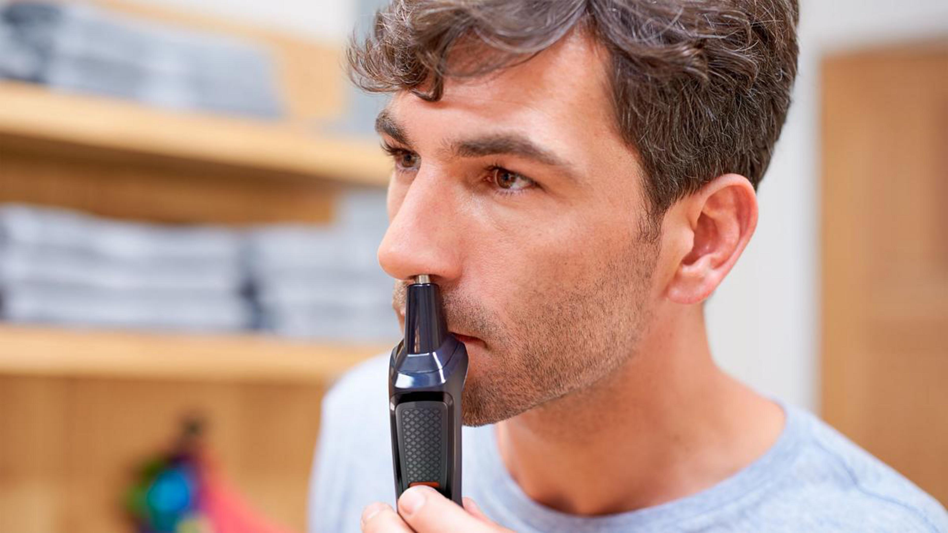 Man using a nose trimmer. Close-up of face and device.