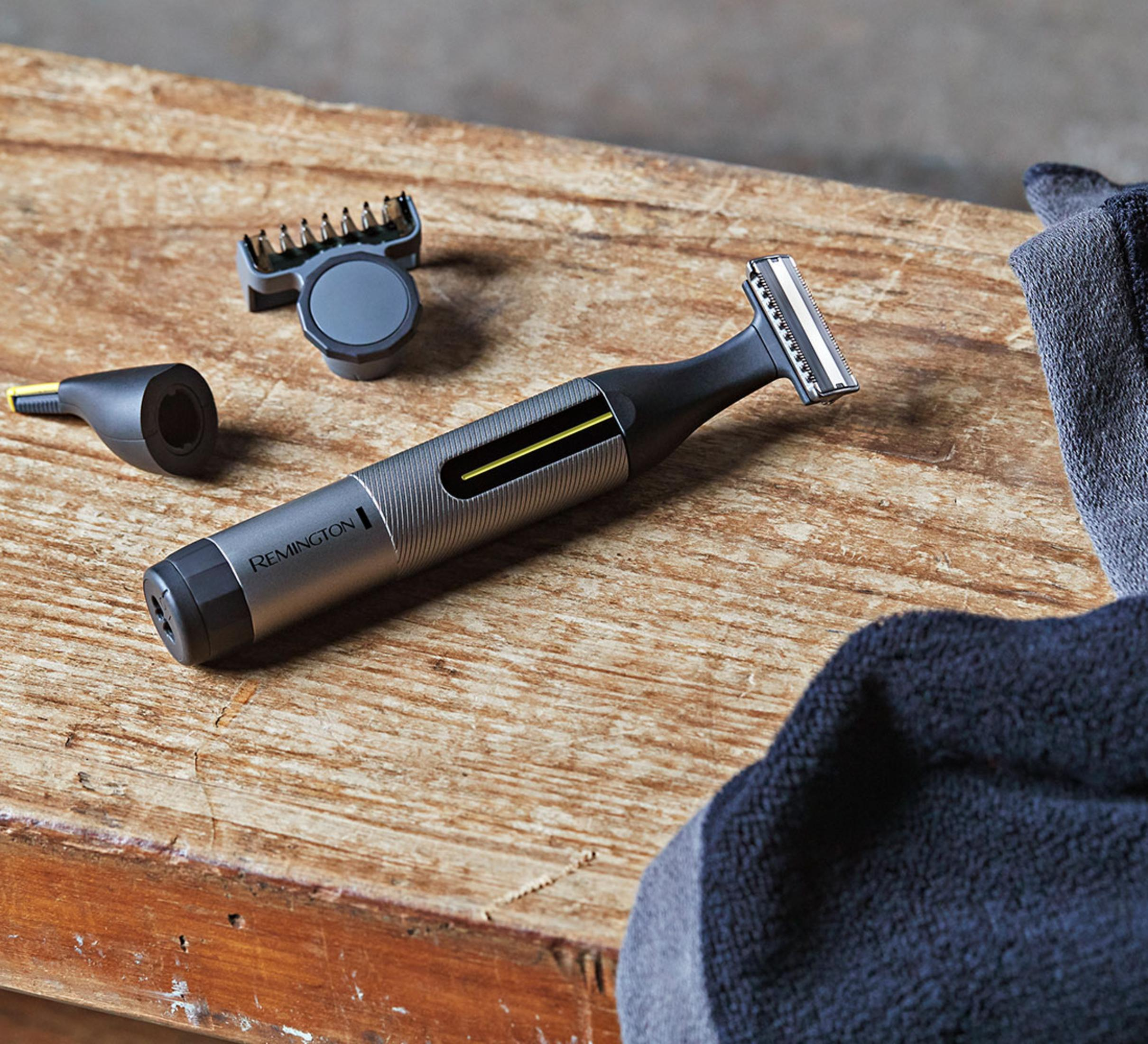 Ein Remington Trimmer mit Aufsätzen und einem dunklen Handtuch auf Holz.