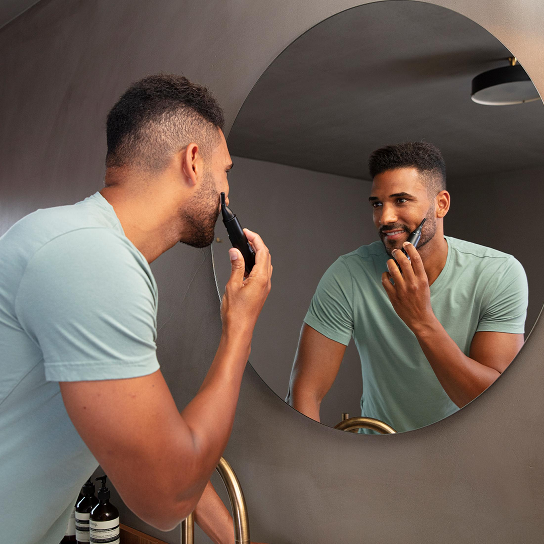 Man trimt zijn baard in spiegel met een zwarte trimmer.