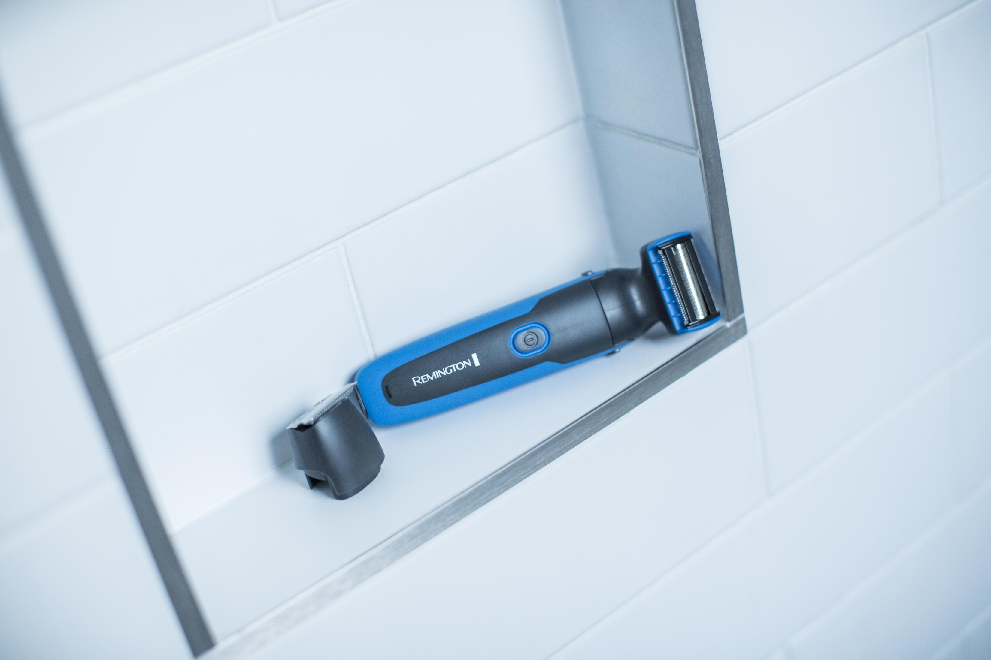Un recortador Remington azul descansa en un nicho con azulejos blancos.
