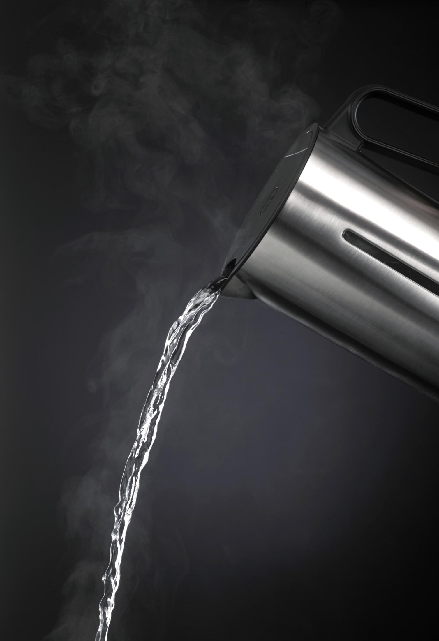 Heißes Wasser wird aus einem silbernen Wasserkocher gegossen, Dampf steigt auf.