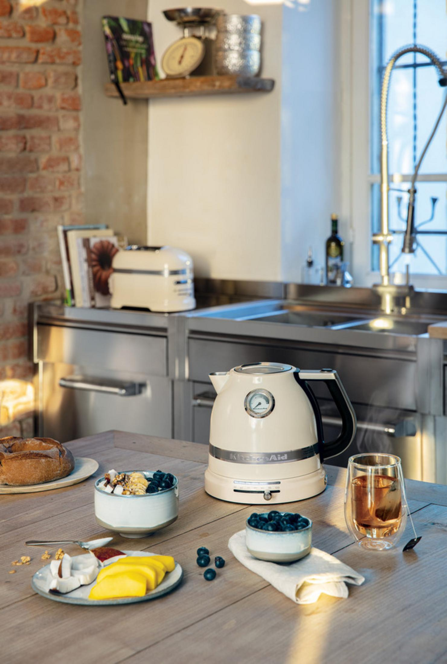 Kremowy czajnik stoi na drewnianym stole z produktami śniadaniowymi.