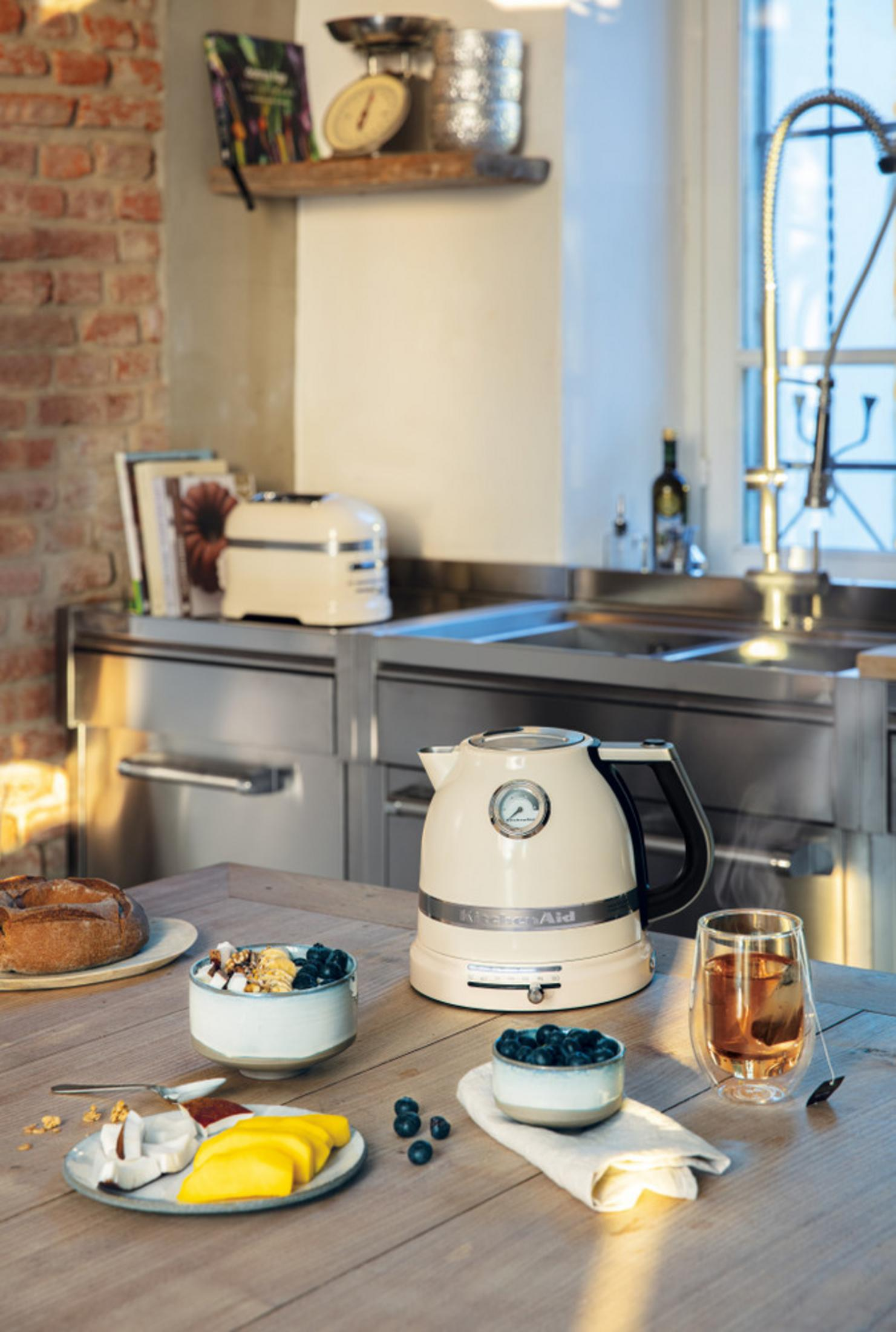 Kremowy czajnik stoi na drewnianym stole obok miski z jagodami.