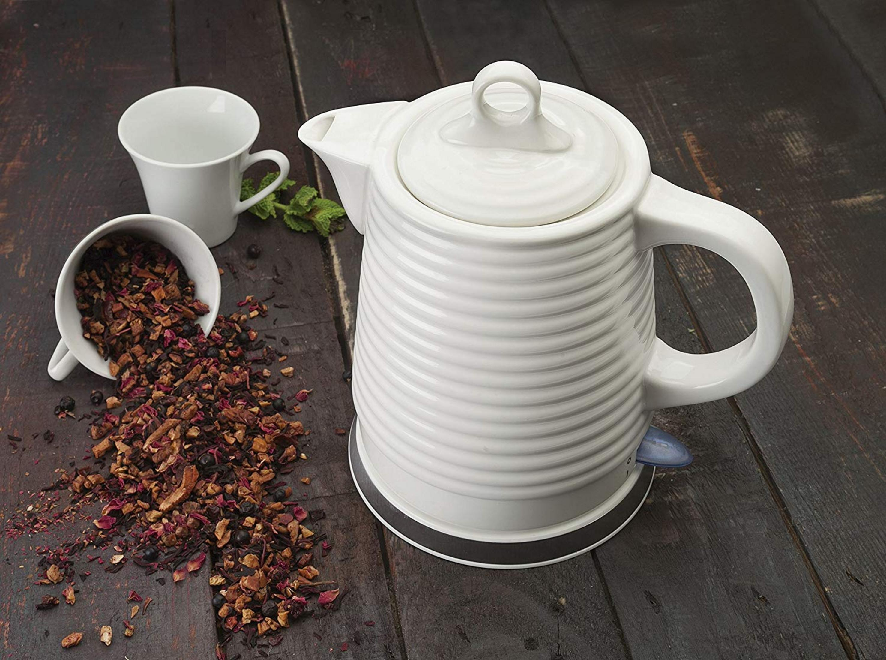 Una tetera blanca con tazas de té y té suelto en mesa de madera.
