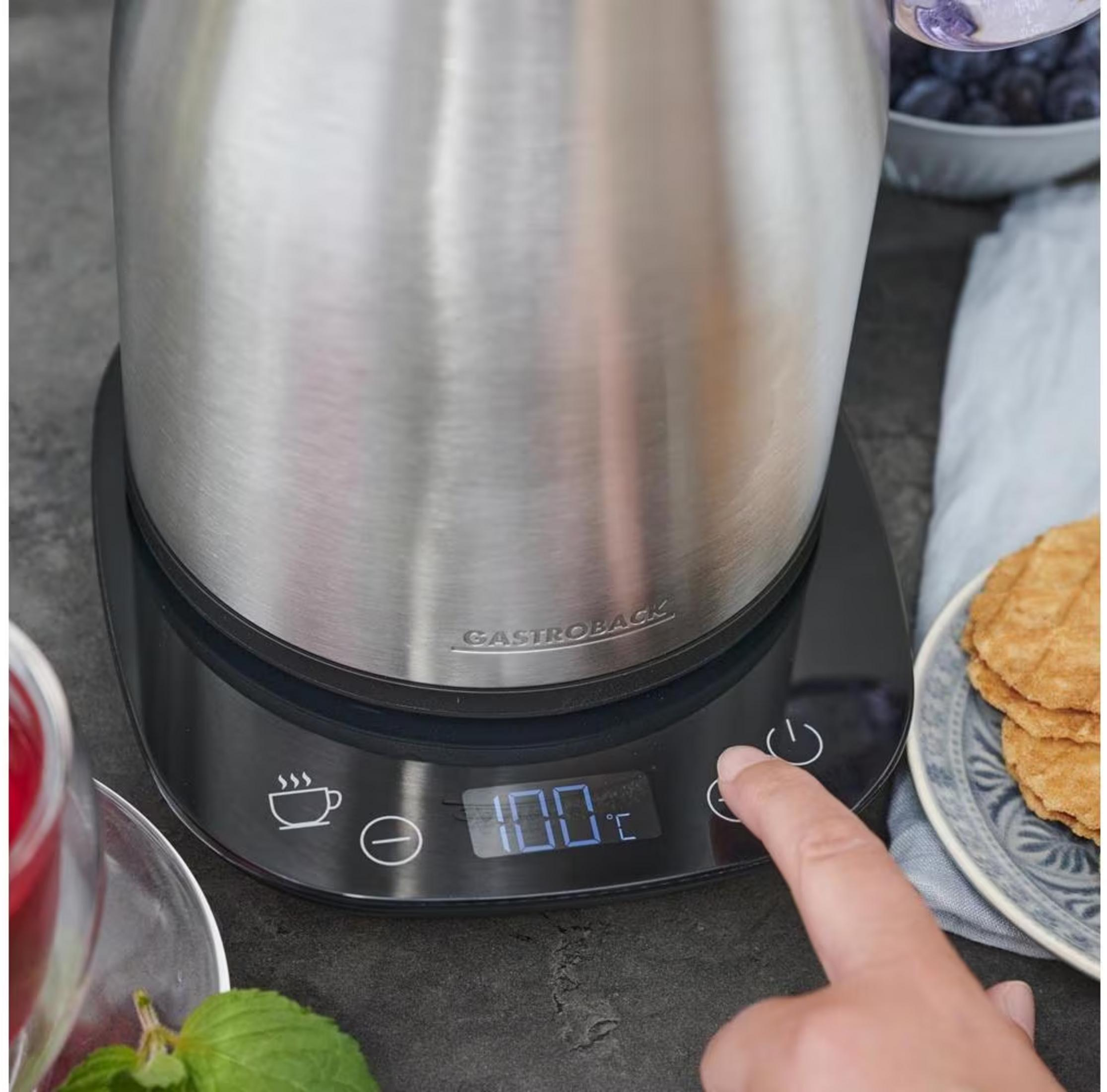 Eine Hand drückt die 100°C-Taste auf einem Wasserkocher-Display.