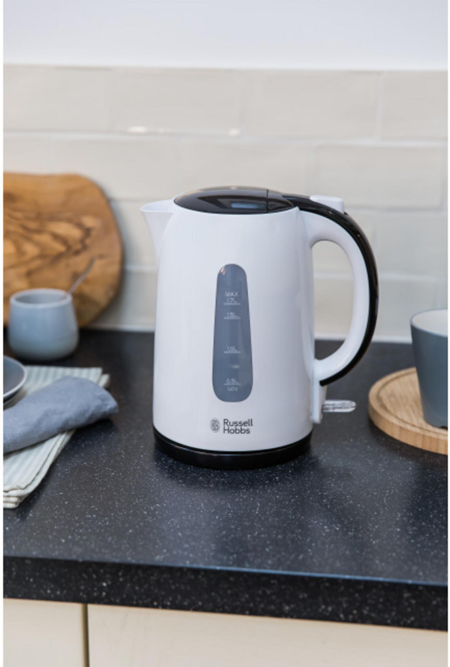 Biały czajnik z czarną rączką i pokrywką stoi na blacie.