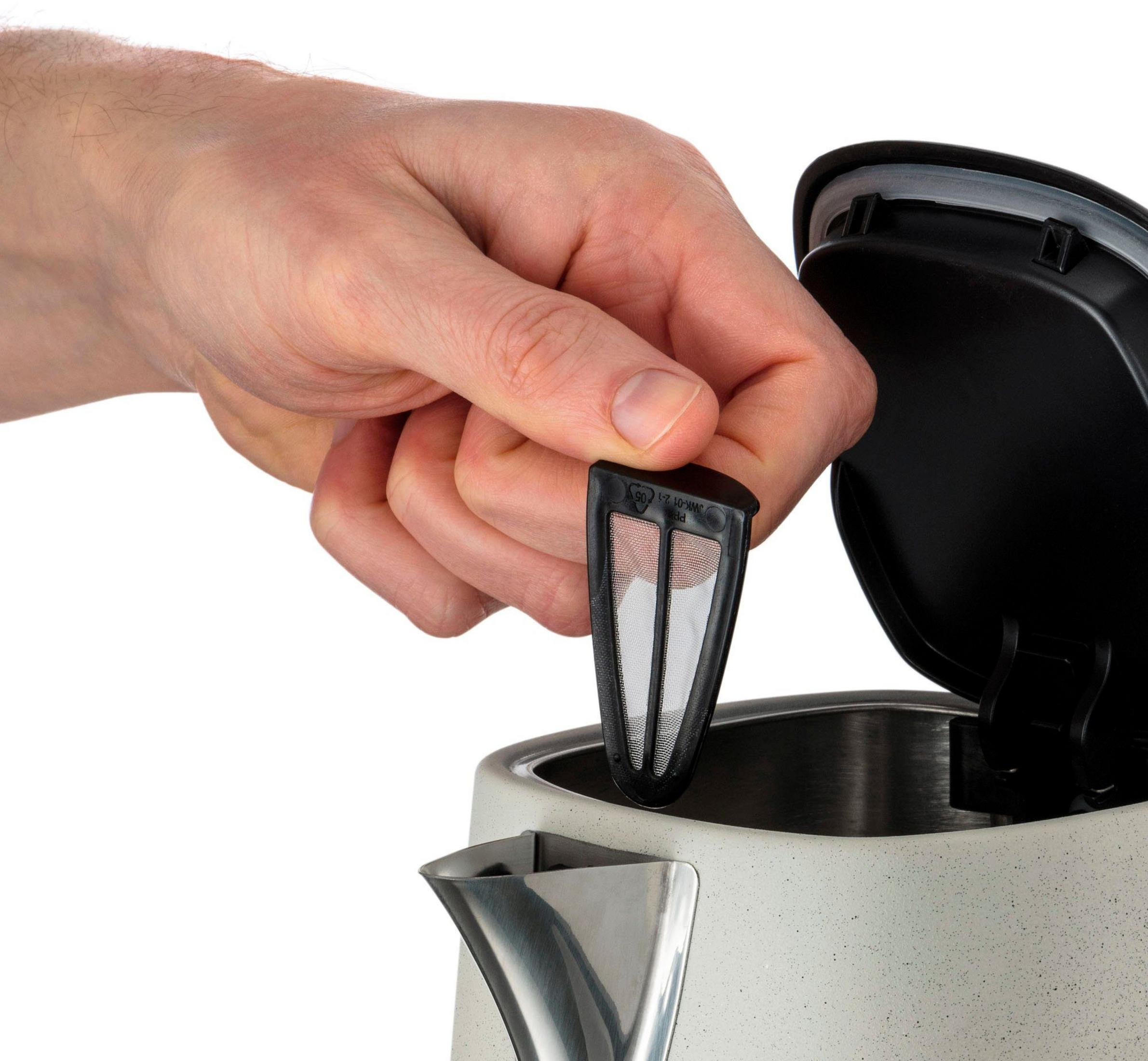 Dłoń trzyma czarny filtr do herbaty nad jasnoszarym czajnikiem.