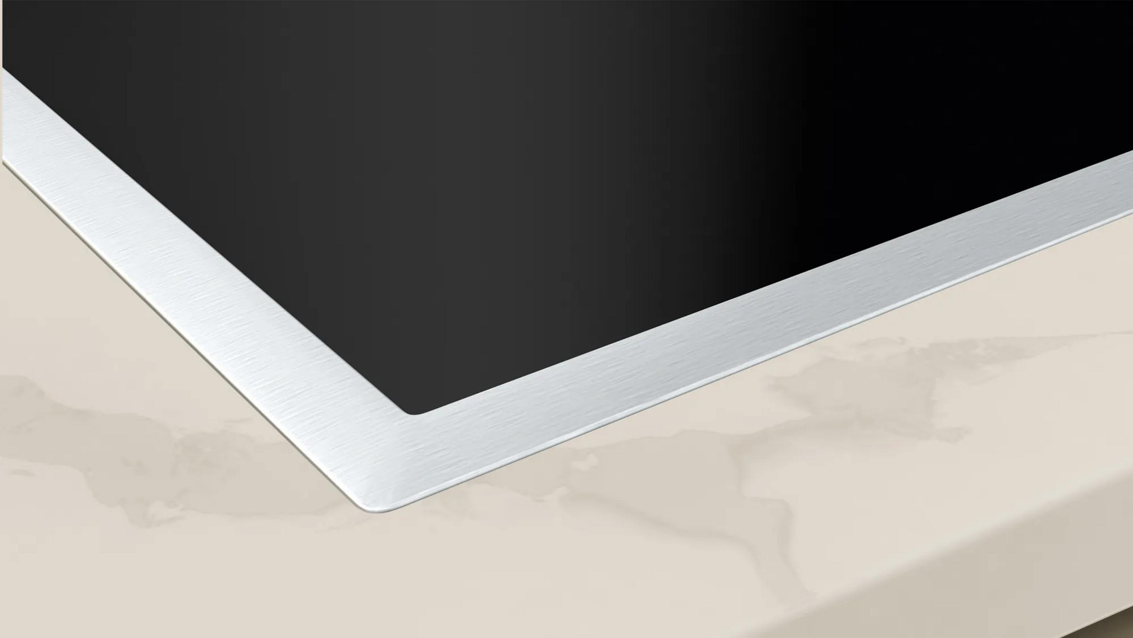 Czarna płyta indukcyjna z srebrną ramką na beżowym blacie.