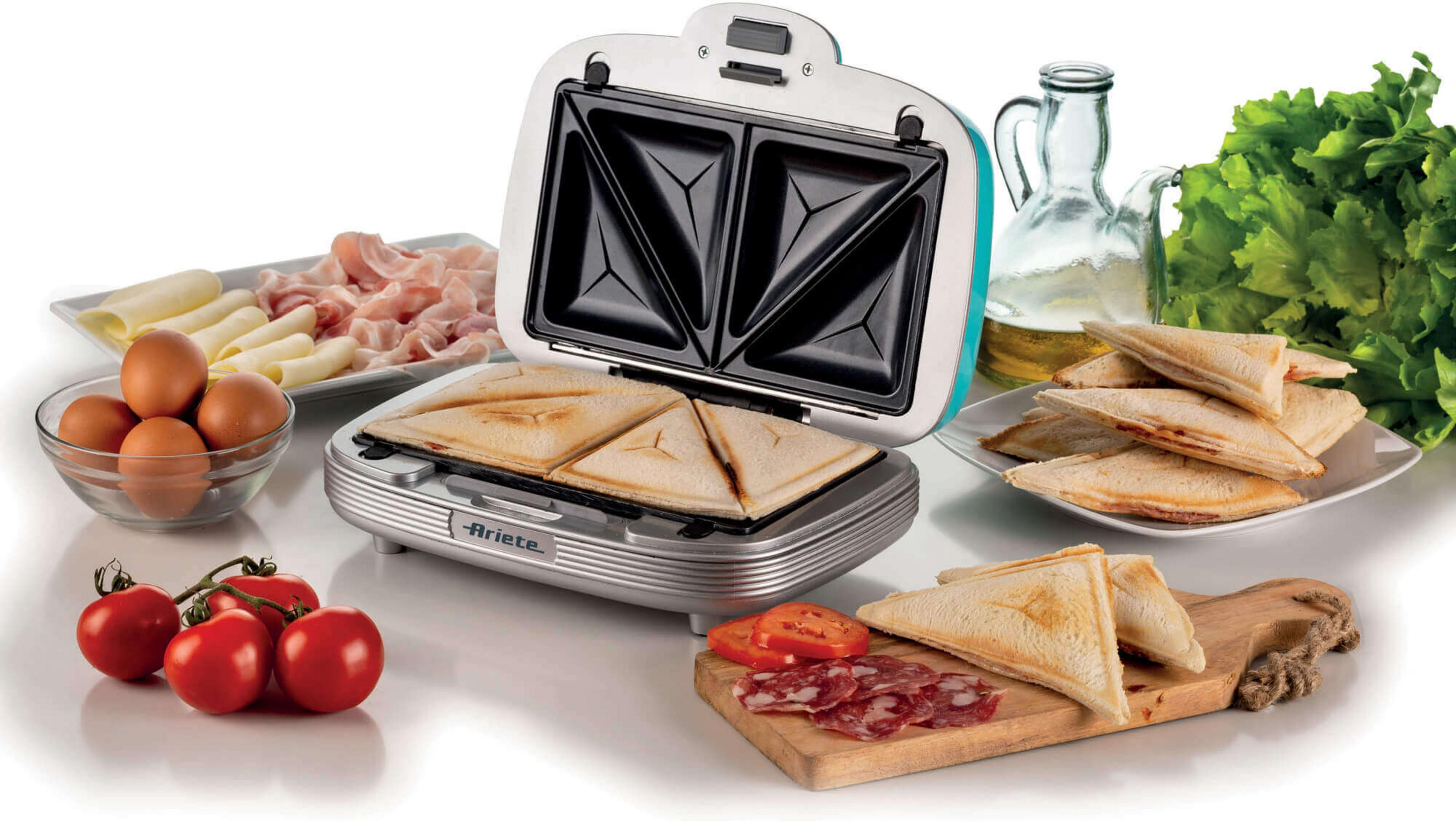 Opiekacz do kanapek z tostami, jajkami, szynką, serem, pomidorami, salami, oliwą i sałatą.