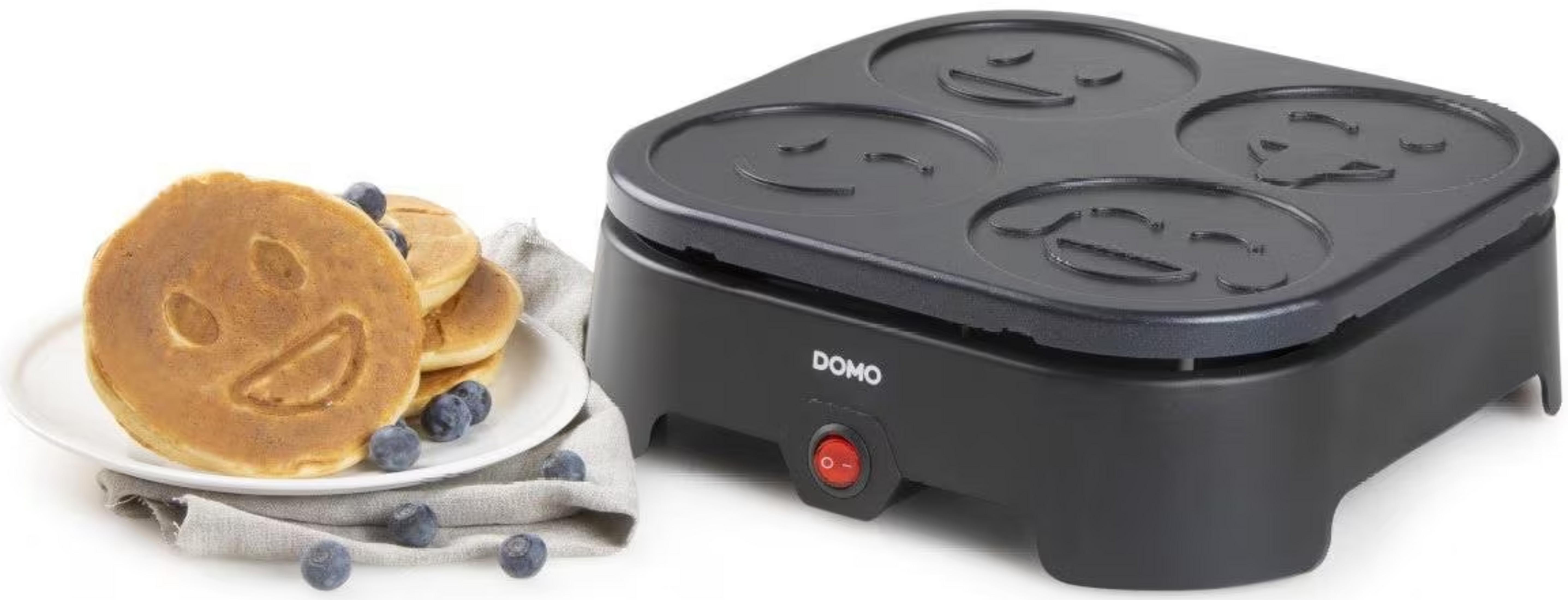 Czarna maszynka do naleśników Domo z 4 foremkami uśmiechniętych buziek i talerzem naleśników.