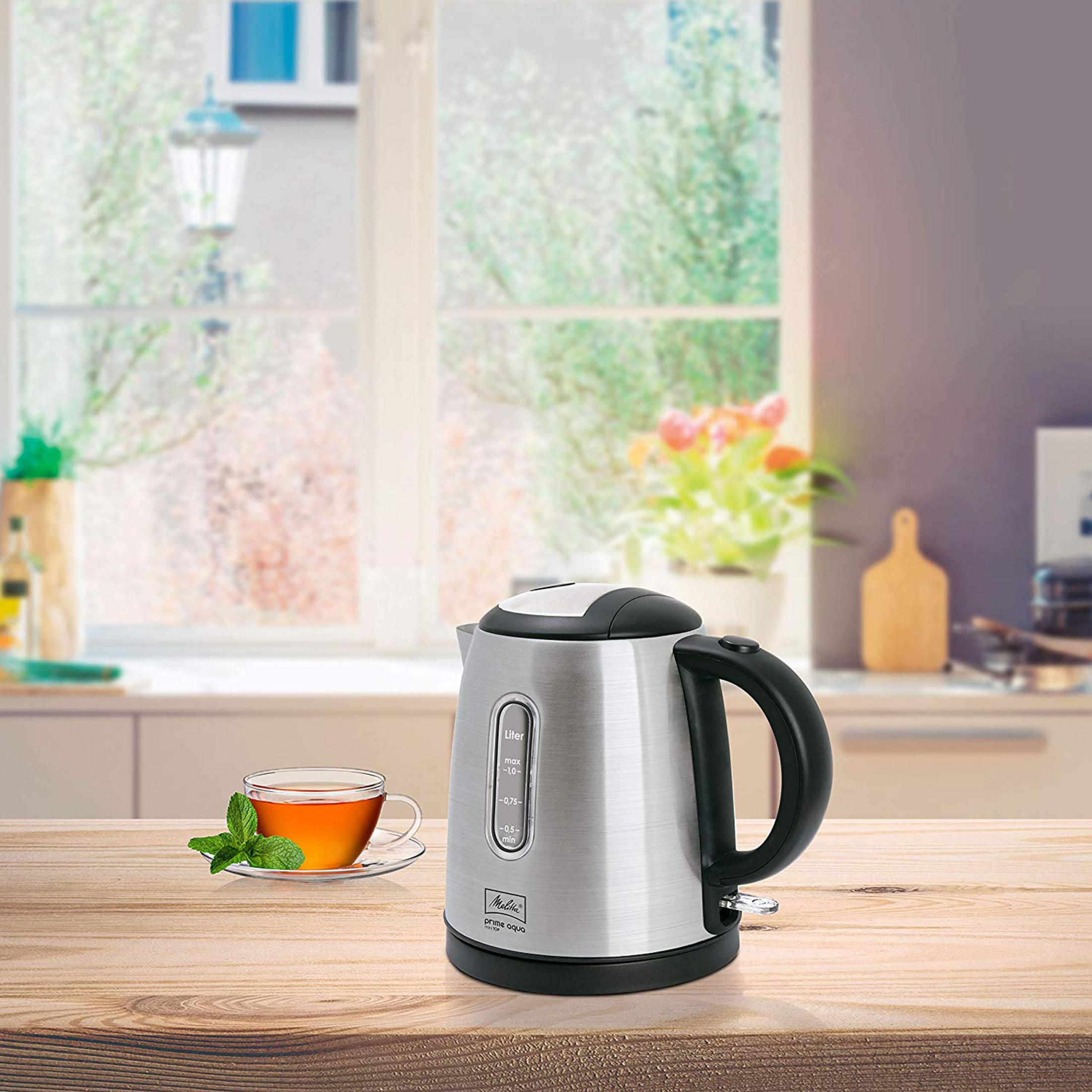 Ein silberner Wasserkocher mit schwarzem Griff steht auf einem Holztisch neben einer Tasse Tee.