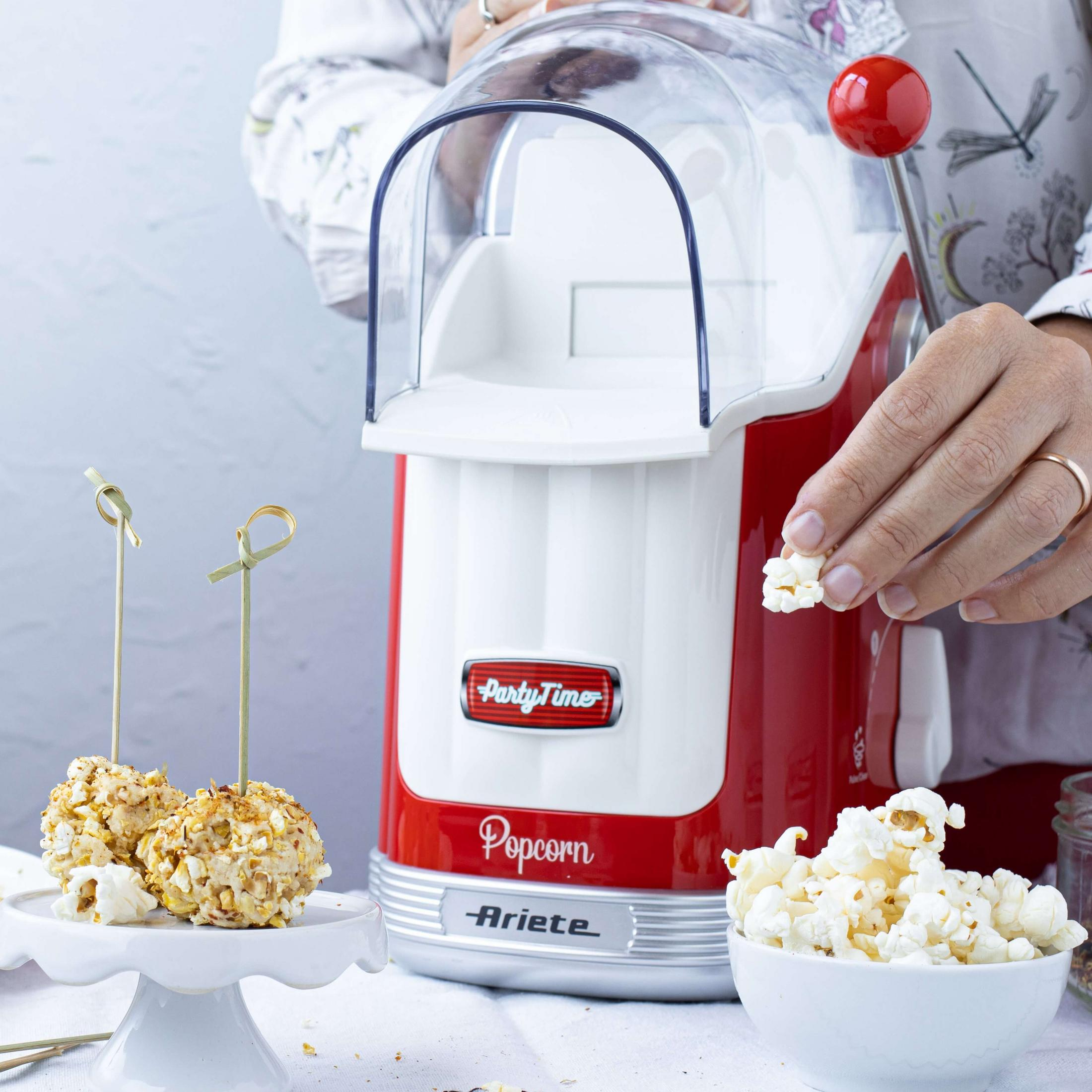 Een persoon houdt popcorn vast naast een rode en witte popcornmachine.